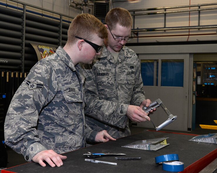 U.S. Air Force Airman 1st Class Cody Leaders, right, 100th Maintenance Squadron Aircraft Structural Maintenance technician from Elizabeth, Colo., shows U.S. Air Force Airman 1st Class Donavan Jerles, left, 100th MXS Aircraft Structural apprentice from Gulf Shores, Ala., how to adjust a saw June 3, 2015, on RAF Mildenhall, England. The hack saw is placed in the holder to create tension on the blade so it doesn’t bow. The Airman used the saw to cut the core straight and level with the surface of the panel. (U.S. Air Force photo by Gina Randall/Released)