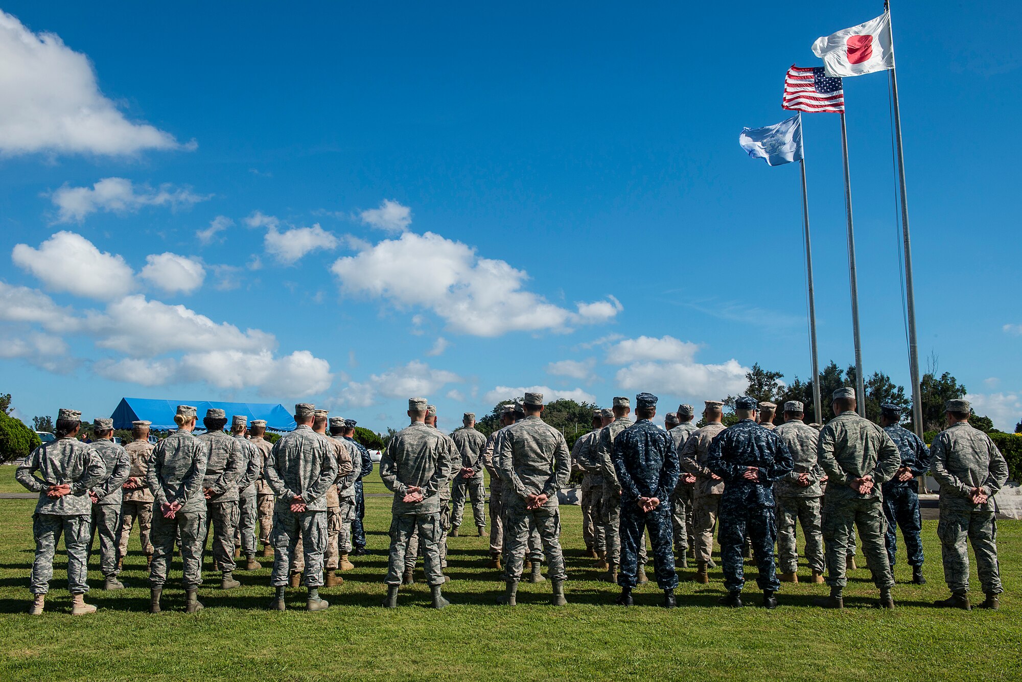 A joint service formation stands at parade rest before the start of the Flag Day ceremony on Kadena Air Base, Japan, June 15, 2015. The ceremony included a decommissioning of an American flag by honor guard personnel, which was retired along with other flags toward the end of the event. Retired flags are destroyed according to the United States Flag Code which states, "The flag, when it is in such condition that it is no longer a fitting emblem of display, should be destroyed in a dignified way, preferably by burning. (U.S. Air Force photo by Senior Airman Stephen G. Eigel)