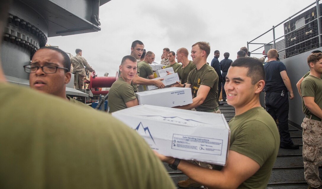 U.S. Marines and Sailors with the 15th Marine Expeditionary Unit and the Essex Amphibious Ready Group assist with offloading packages aboard the USS Rushmore (LSD 47) during a replenishment at sea in the South China Sea, June 14, 2015. Marines and sailors with the 15th MEU, and Essex ARG worked together to off load food, maintenance parts, and letters from home. (U.S. Marine Corps photo by Sgt. Emmanuel Ramos/Released)