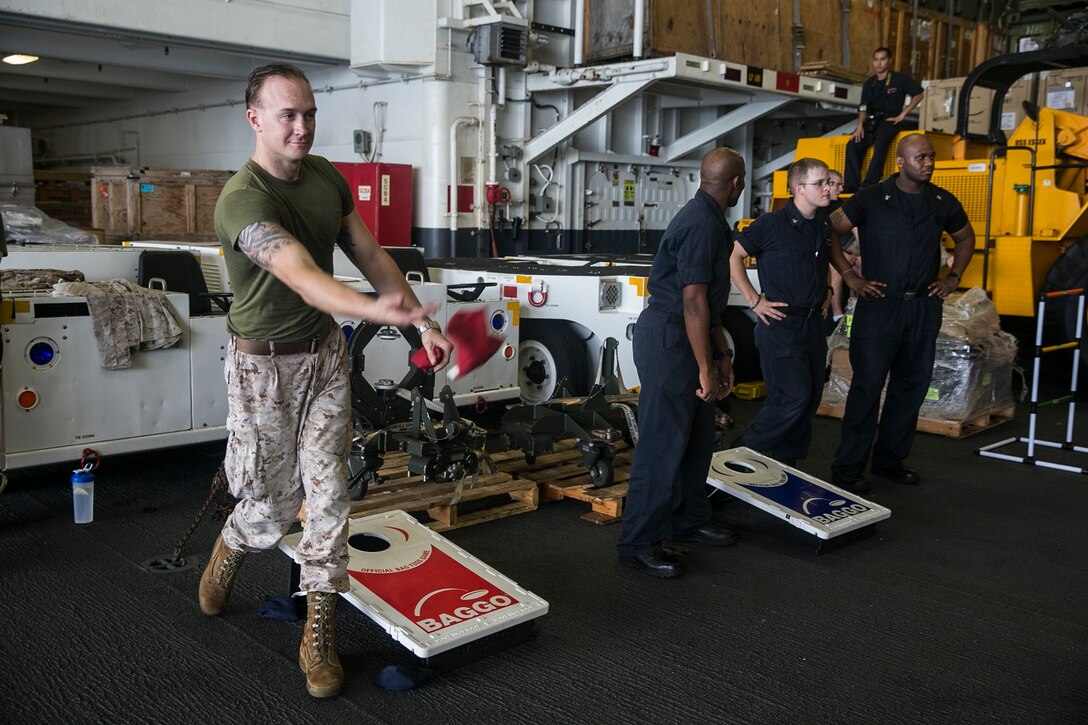 U.S. Marine Sgt. Douglas Bobo, left, tosses a bean bag during a game of corn hole in the hangar bay of the USS Essex (LHD 2) at sea in the Strait of Malacca, June 15, 2015. Bobo is a member of the 15th Marine Expeditionary Unit’s Command Element. The Marines and Sailors aboard the USS Essex enjoyed a “Steel Beach,” which consisted of grilling, music, and games. (U.S. Marine Corps photo by Cpl. Anna Albrecht/Released)