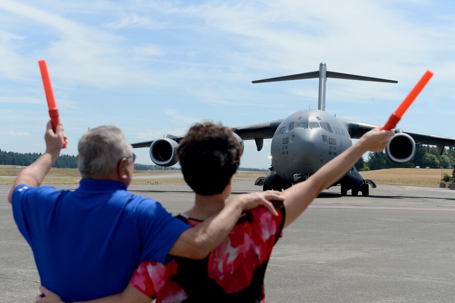 Tom and Carolyn Kumashiro, parents of Col. David Kumashiro, 62nd Airlift Wing commander, guide a C-17 Globmaster III while Kumashiro taxis in June 15, 2015, at Joint Base Lewis-McChord, Wash. After parking, Kumashiro’s family was able to spray him with champagne and water. (U.S. Air Force photo/Airman 1st Class Keoni Chavarria)