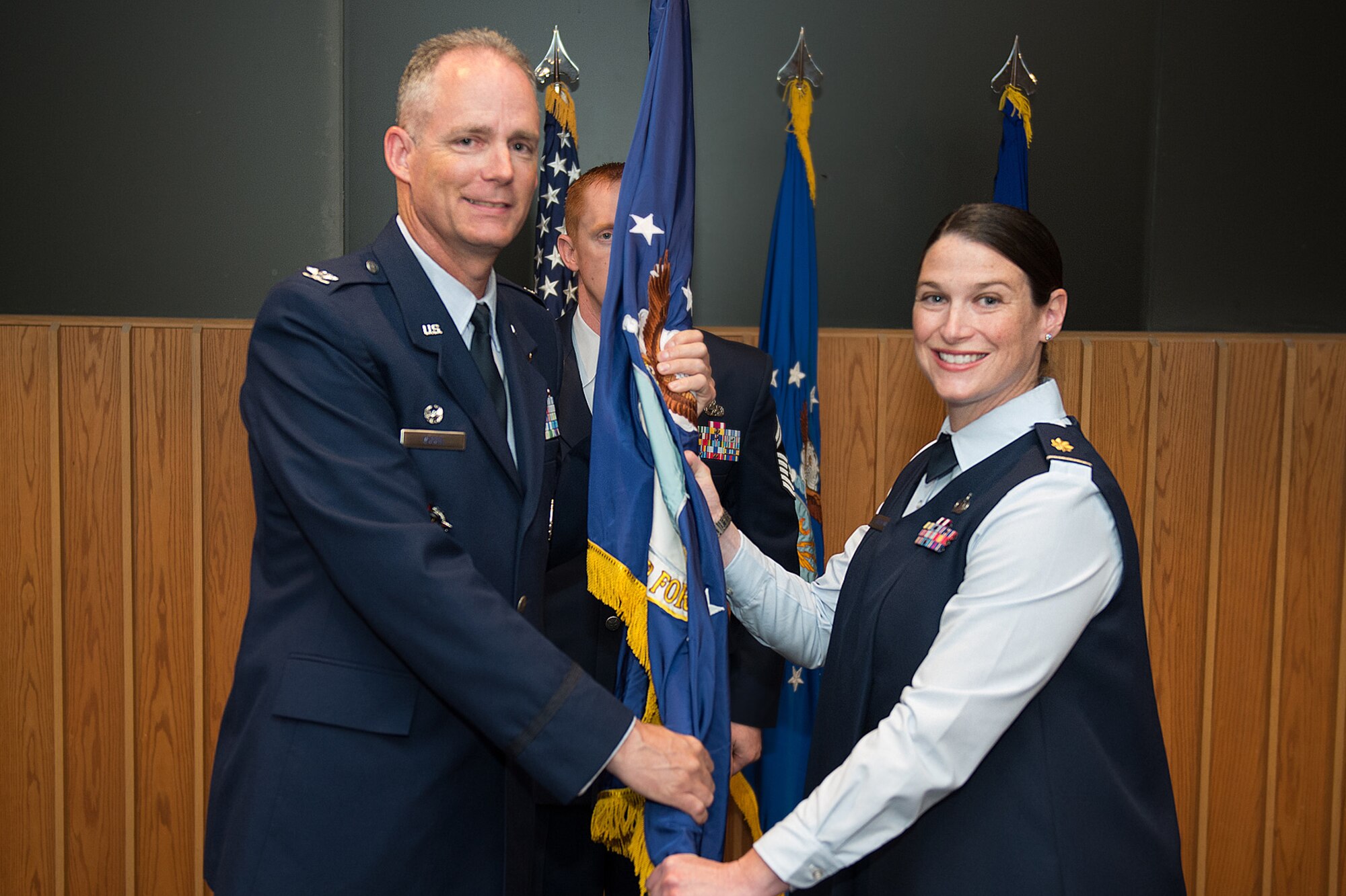 Col. Michael A. Vogel, installation commander, passes the flag to Maj. Maria T. Beecher, Air Force Life Cycle Management Center Detachment 7 commander, during a change of command ceremony July 8 in the O'Neil Auditorium. The commander is responsible for advising AFLCMC-Hanscom program executive officers on military personnel management and providing administrative control over members to include overseeing deployments, training, fitness, medical evaluations and discipline. (U.S. Air Force photo by Rick Berry) 