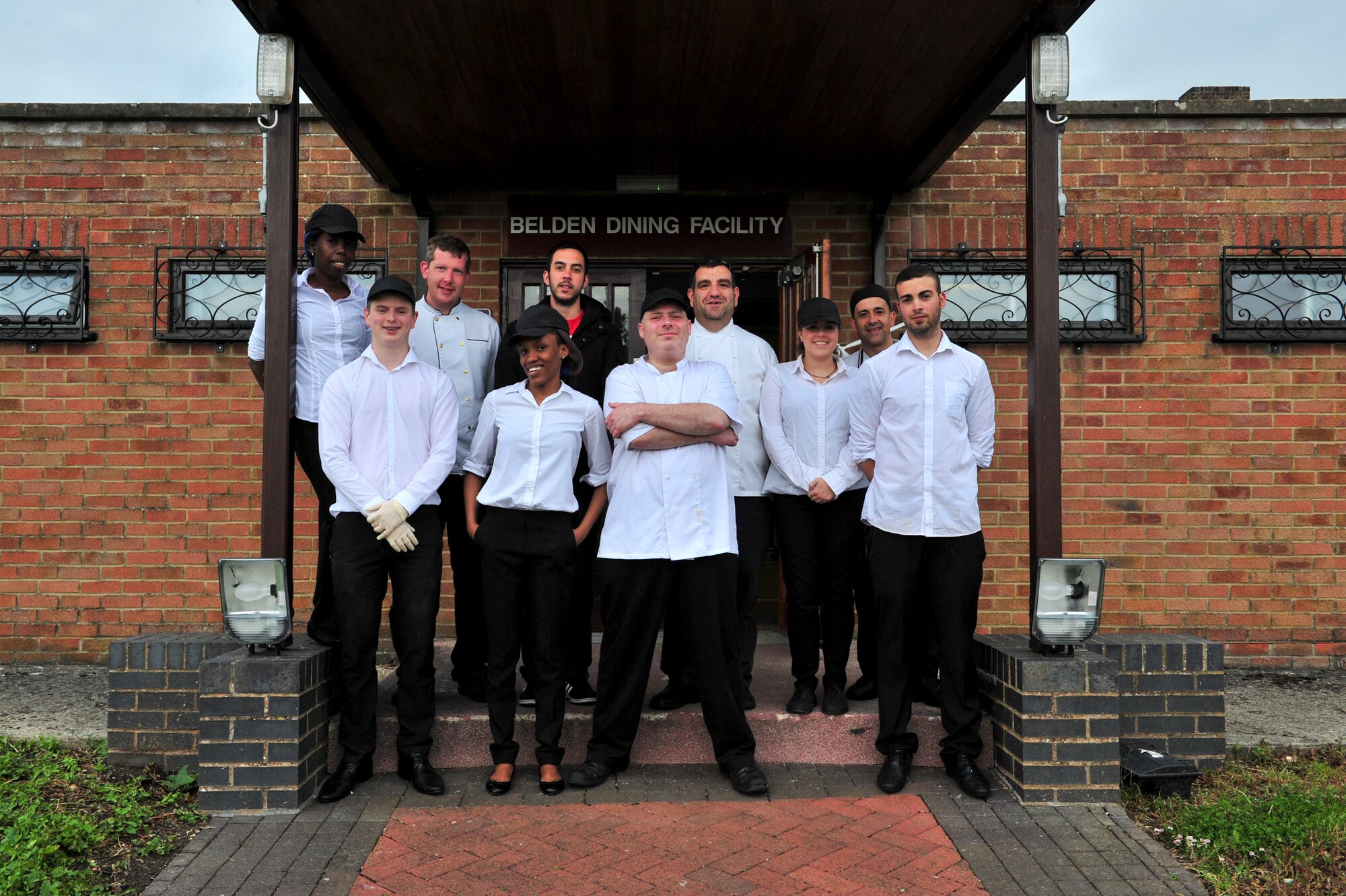 Staff members contracted from the local area pose for a photo in front of the dining facility at Royal Air Force Fairford, England, June 14, 2015. RAF Fairford is considered a “warm” base maintained by the U.S. Air Force. With an approximately 10,000-foot runway and its proximity to Royal Air Force Welford, the base has a unique and versatile capability and is an ideal training area for large-scale exercises. The base was transformed from “warm” status to active status in support of the BALTOPS 15 and Saber Strike 15 exercises. (U.S. Air Force photo/Senior Airman Malia Jenkins) 