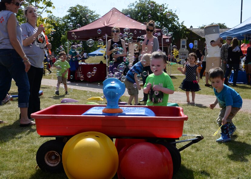 Team Mildenhall children play with a bubble machine during the Marauder Melee June 11, 2015, on RAF Mildenhall, England. The day began with fitness competitions and ended with an open to all event in Washington Square with events such as a petting zoo, multiple bouncy attractions and Segway rides. (U.S. Air Force photo by Gina Randall/Released)