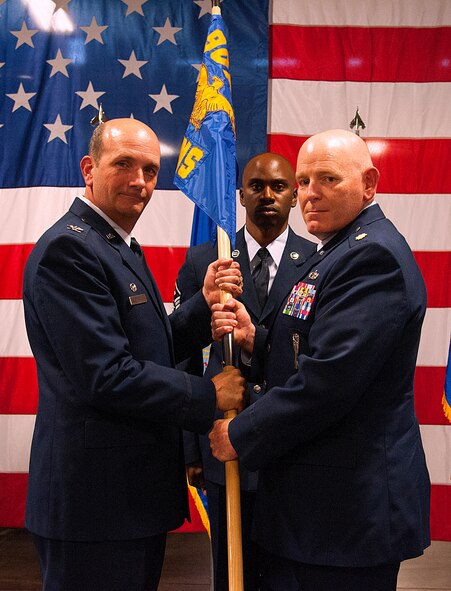 Col. Trevor Flint, 90th Maintenance Group commander, passes the guidon to Maj. Kevin Barber, 90th Munitions Squadron commander, during the 90th MUNS change-of-command ceremony June 17, 2015, as Master Sgt. Christopher Stokes, 90th MUNS first sergeant, stands in the background in the 90th MXG High Bay on F.E. Warren Air Force Base, Wyo. The ceremony signified the transition of command from Maj. Stephanie Wilson to Barber. (U.S. Air Force photo by Senior Airman Jason Wiese)
