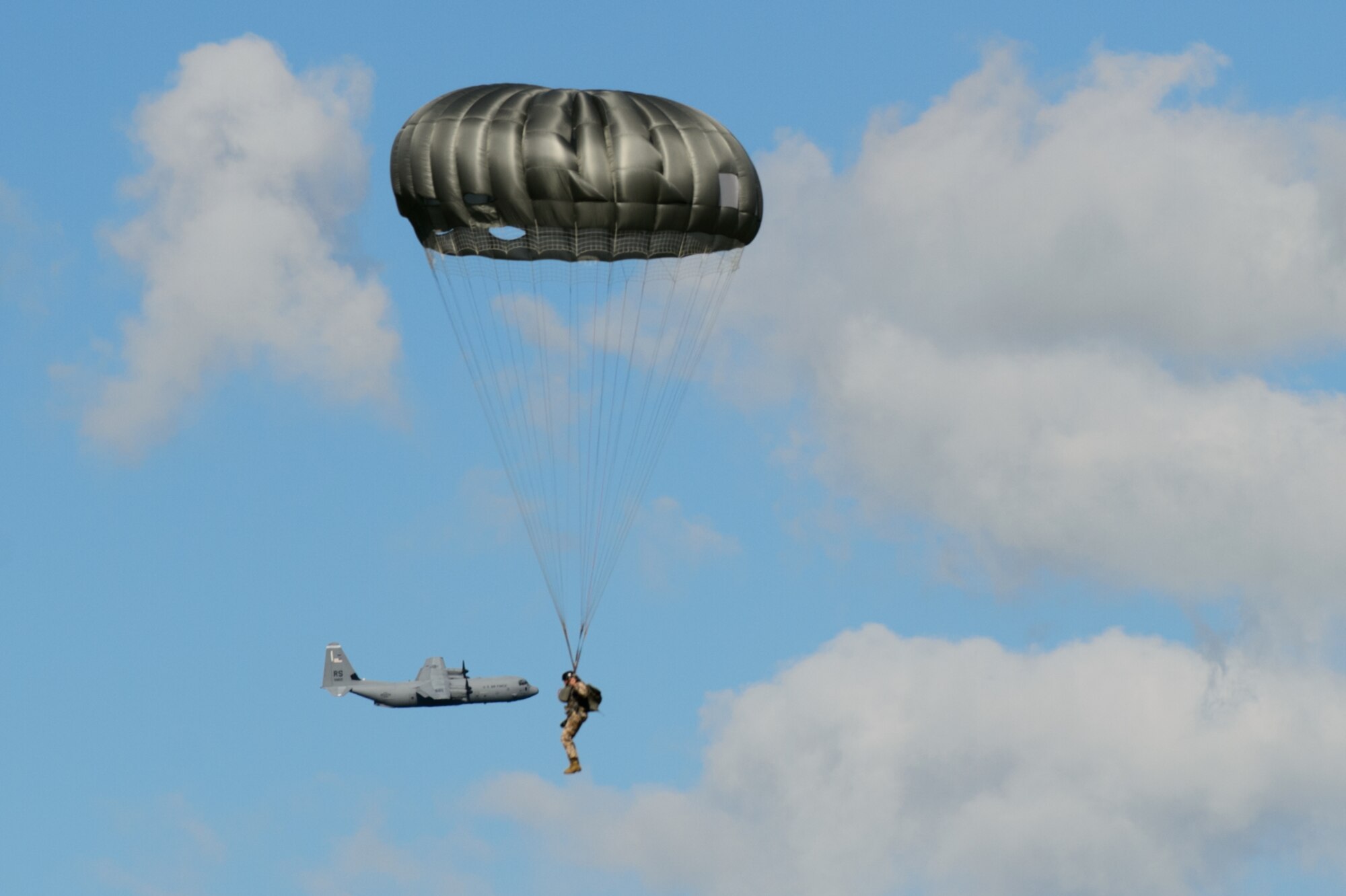 A C-130J Super Hercules passes behind a Latvian military member during a combined jump day June 15, 2015, Lielvarde Air Base, Latvia. More than 70 U.S. Air Force, U.S. Army and Latvian service members participated in a jump day to strengthen the bonds of allies and learn from each other during exercise Saber Strike 15. The exercise involves more than 6,000 service members from 14 nations participation all throughout Estonia, Latvia, Lithuania, and Poland to learn from each other and promote stability is the region. (U.S. Air Force photo/ Staff Sgt. Armando A. Schwier-Morales)