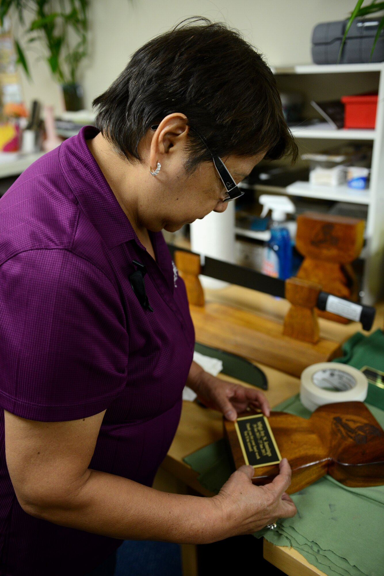 Ofelia Regis, 36th Force Support Squadron Arts and Crafts Center recreation assistant, centers a name plate on an award June 10, 2015, at Andersen Air Force Base, Guam. The Arts and Crafts Center provides engraving and framing services as well as a wide variety of classes for people of all ages. (U.S. Air Force photo by Airman 1st Class Arielle Vasquez/Released)