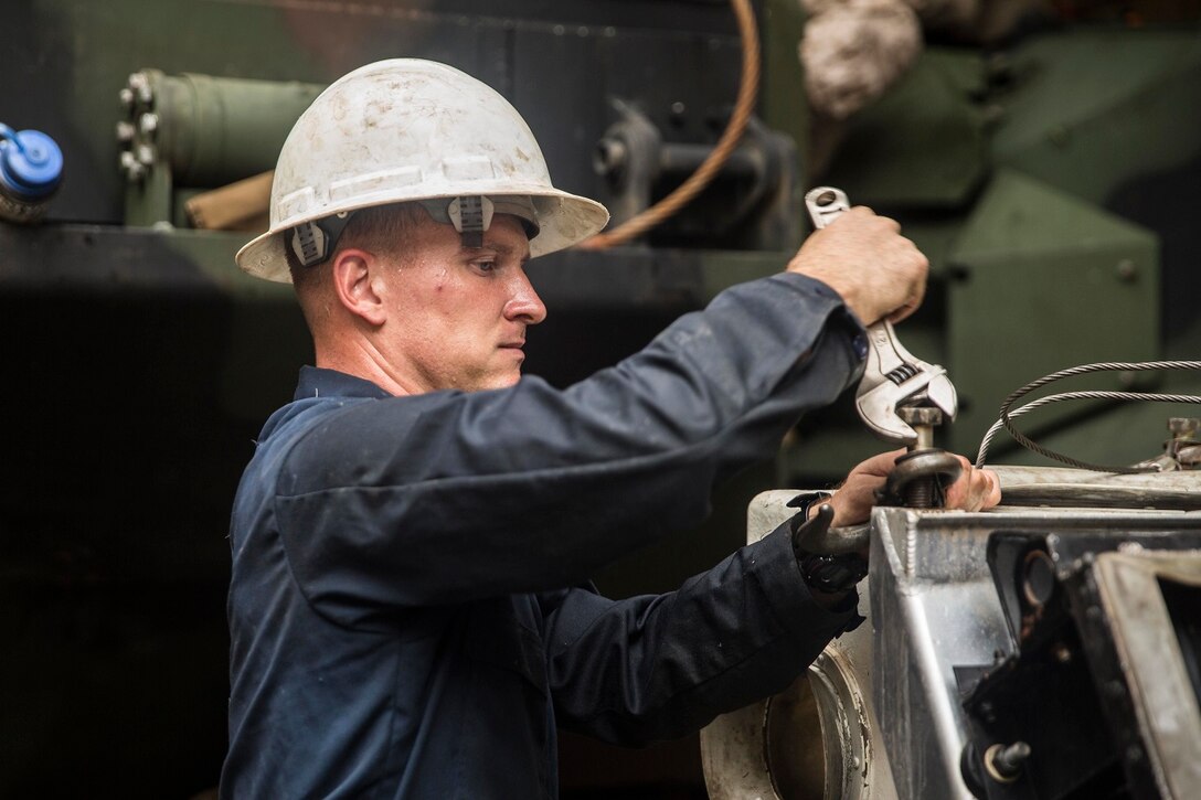 U.S. Marine Sgt. Brandon Combs loosens bolts on a coolant tower of an AAV-7 Amphibious Assault Vehicle during vehicle maintenance aboard USS Rushmore (LSD 47) at sea in the Strait of Malacca, June 15, 2015. Combs is an assistant maintenance chief with Kilo Company, Battalion Landing Team 3rd Battalion, 1st Marine Regiment, 15th Marine Expeditionary Unit. AAV crewmen were replacing the hydrostatic steering unit, a component that controls the vehicle’s steering. (U.S. Marine Corps photo by Sgt. Emmanuel Ramos/Released)