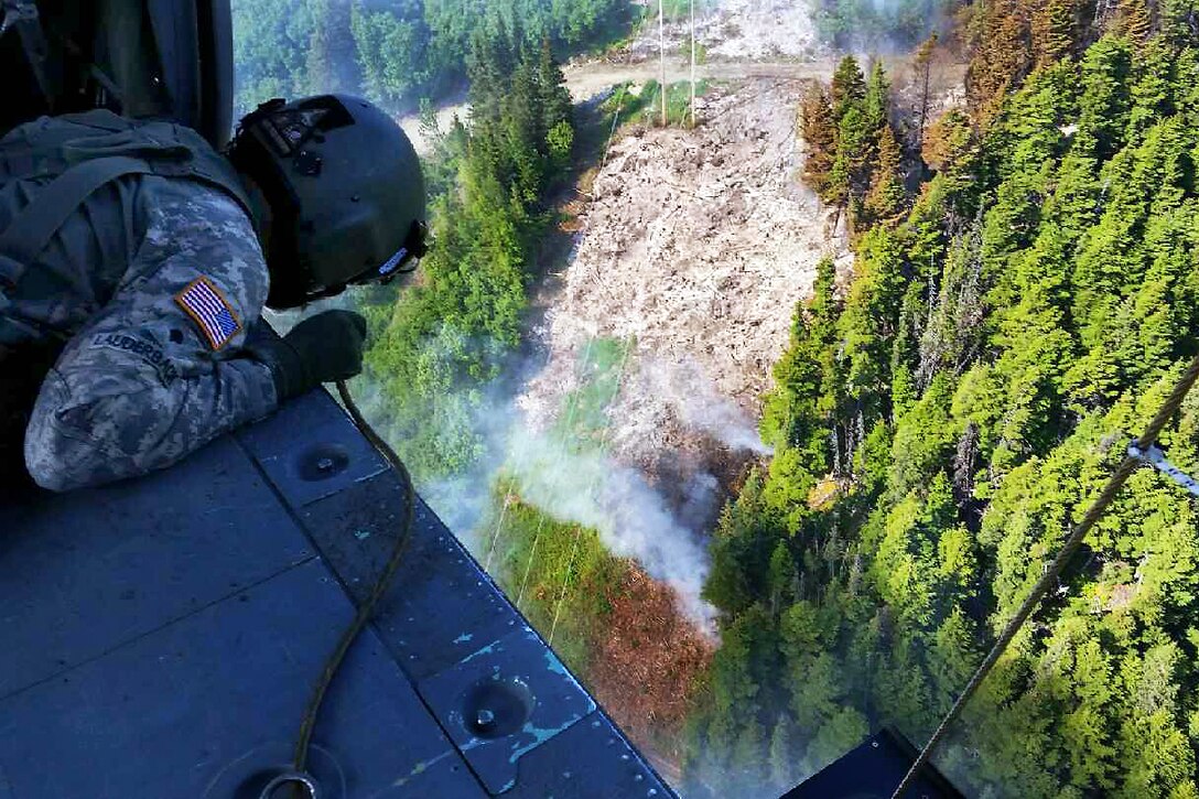 Army Spc. Tanner Lauderback watches water drop from a bambi bucket during firefighting efforts at Russian Lake near Cooper Landing, on the Kenai Peninsula in Alaska, June 17, 2015. Lauderback, a crew chief assigned to the Alaska National Guard's 1st Battalion, 207th Aviation Regiment, flew multiple missions as crews dropped thousands of gallons of water over the fire.