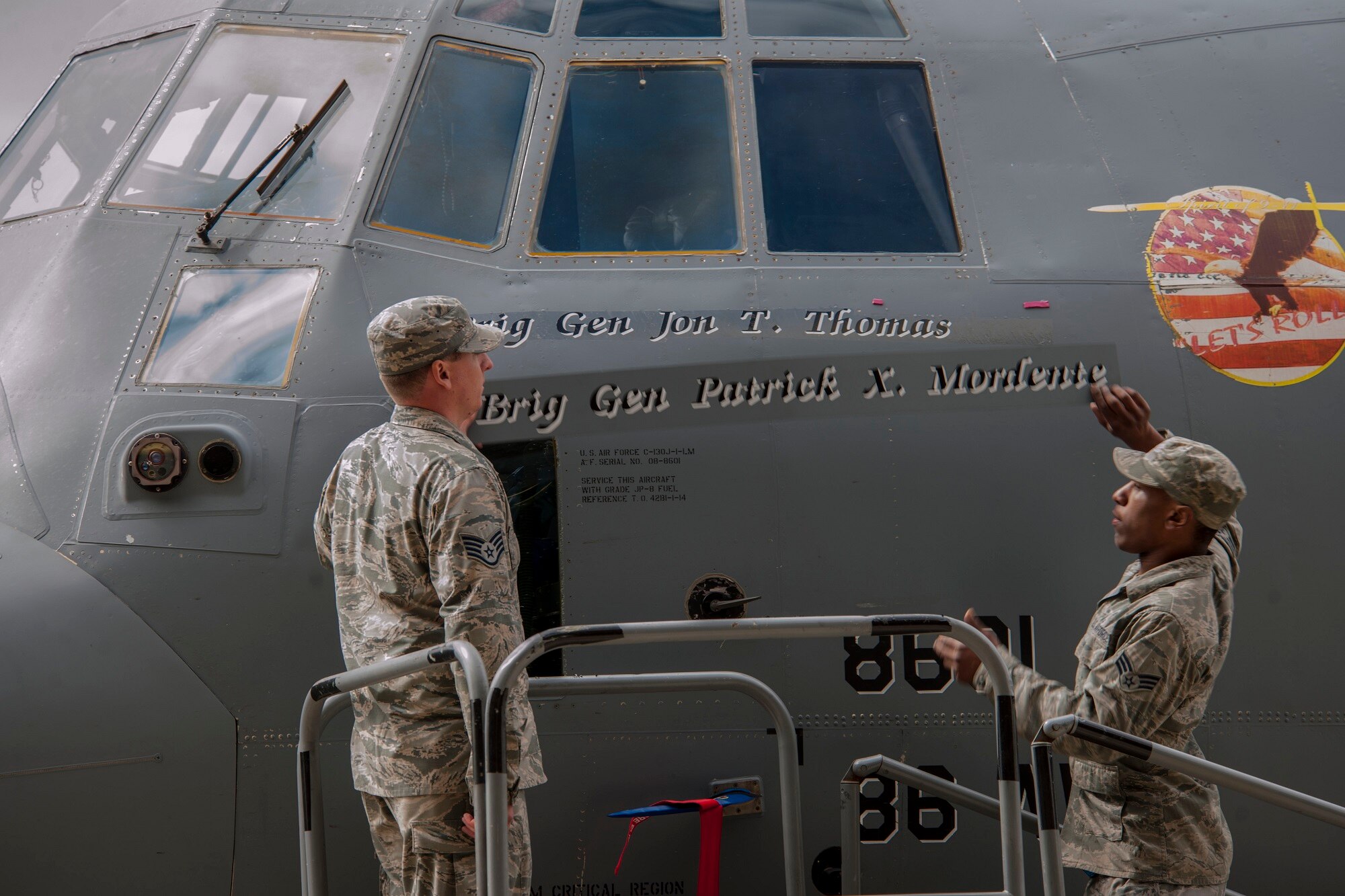 Two Airmen reveal the name of Brig. Gen. Jon T. Thomas, 86th Airlift Wing commander, on the nose of a C-130J Super Hercules during a change of command ceremony June 19, 2015, at Ramstein Air Base, Germany. It is tradition to name an aircraft after the commander of the airlift wing. (U.S. Air Force photo/Airman 1st Class Tryphena Mayhugh)