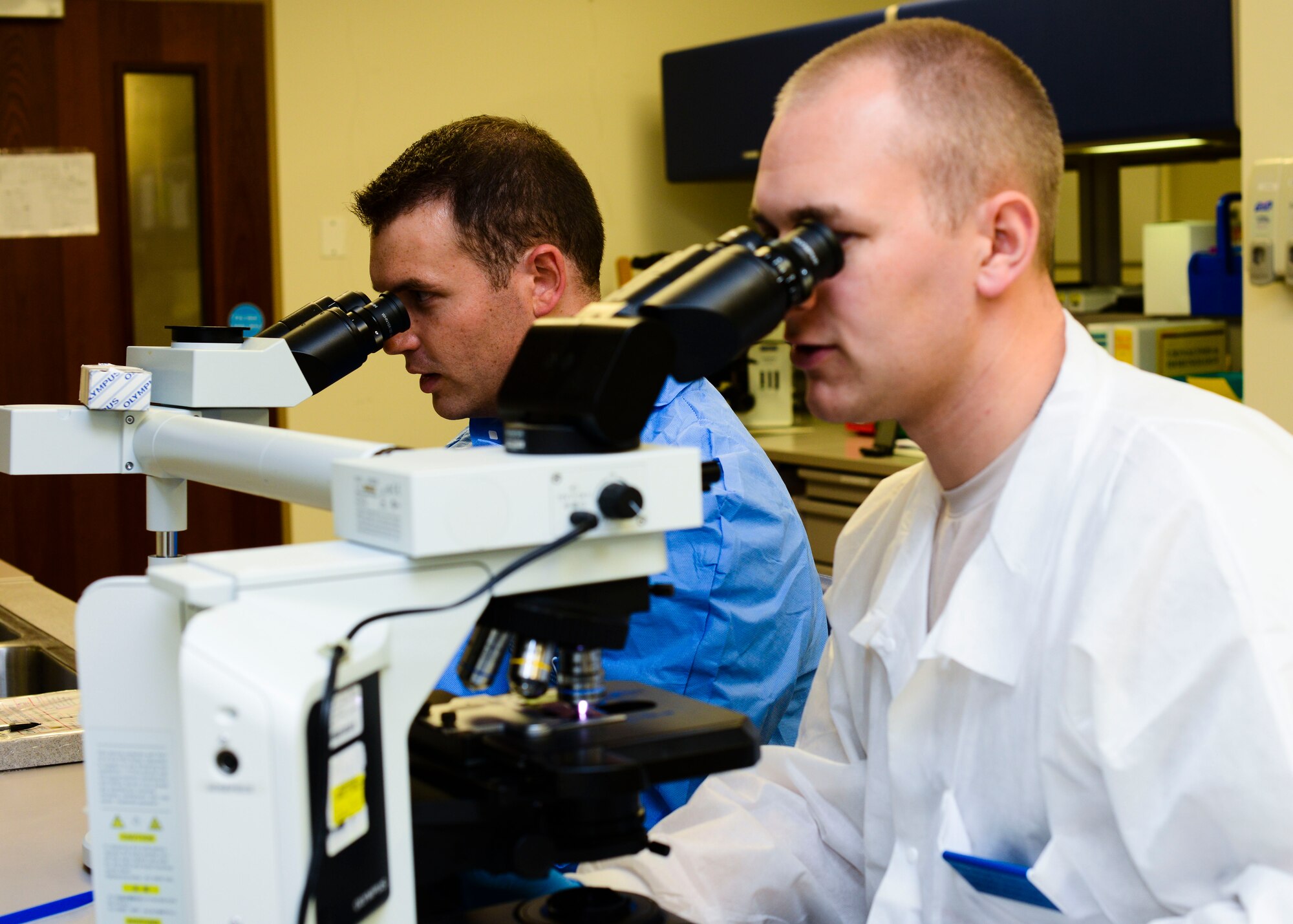 From left, U.S. Air Force Tech. Sgt. Nicholas Igl, 31st Medical Support Squadron laboratory flight chief, and Staff Sgt. Grant Wendland, 31 MDSS medical laboratory technician, view a training slide through a microscope, June 15, 2015, at Aviano Air Base, Italy. Microscopes allow two people to view a slide together for training purposes. (U.S. Air Force photo by Senior Airman Austin Harvill/Released)