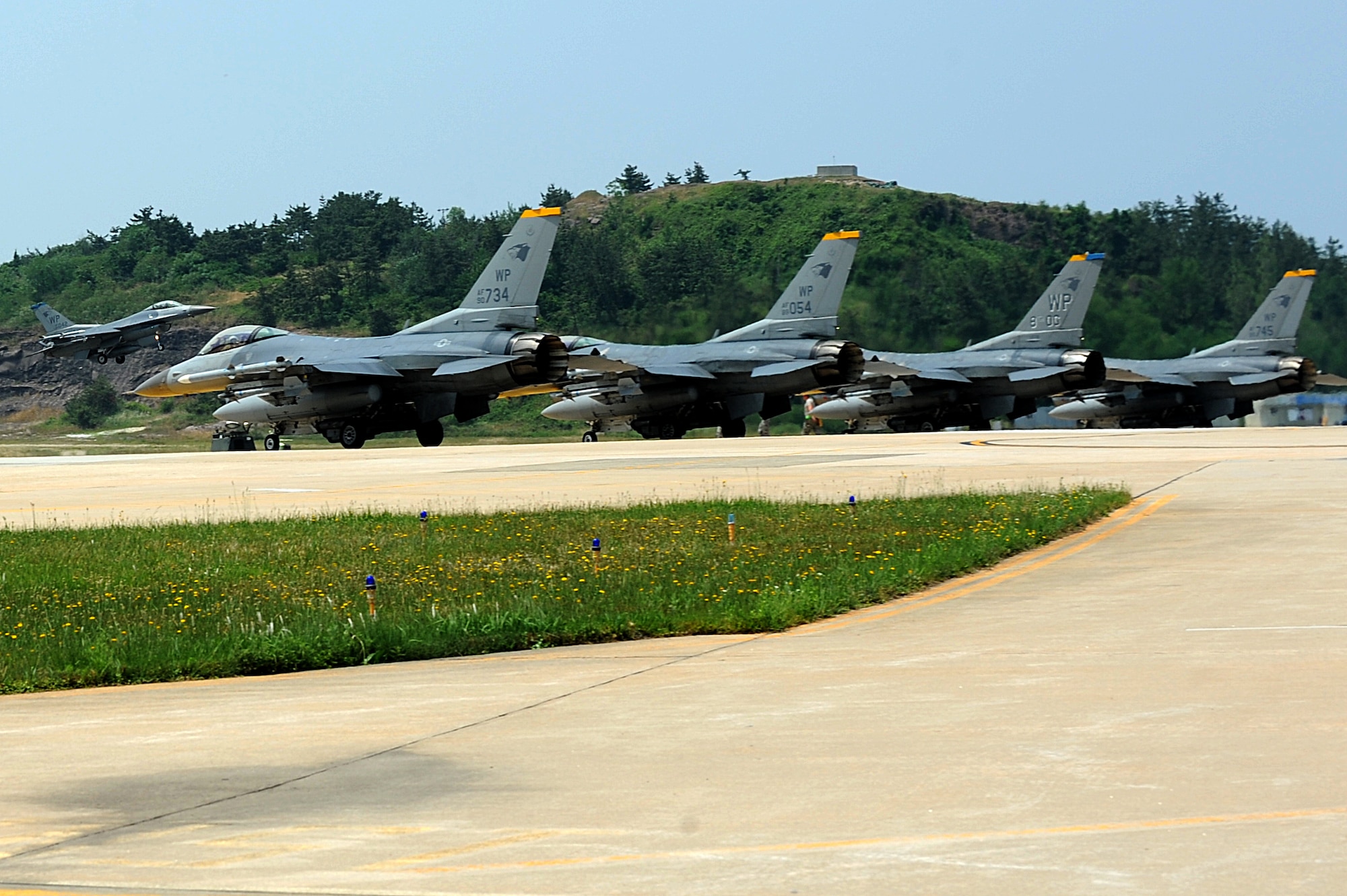 Four F-16 Fighting Falcons line up on the runway before taking off as another F-16 lands during Surge Week at Kunsan Air Base, Republic of Korea, June 18, 2015. Surge Week tested the skills and wartime capabilities of Wolf Pack operators, maintainers and supporting agencies over a four-day window to simulate pilots' wartime flying rates. (U.S. Air Force photo by Senior Airman Divine Cox/Released)