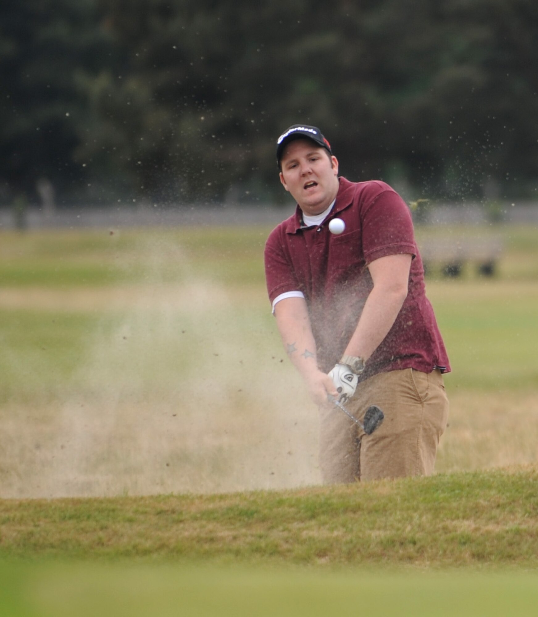 David Busch, 352nd Special Operations Aircraft Maintenance Squadron aero-repair wheel and tire journeyman from Reading, Pa, plays out of the greenside bunker on the 330-yard par 4 first hole during the RAF Mildenhall intramural golf match June 17, 2015, at Breckland Pines Golf Club on RAF Lakenheath, England. The golfers were playing scramble format, where all members of the team hit from the same spot throughout the hole, using the best shot each time to determine the location of the next shot. The “best ball” format continues with each round of shots counting as one stroke for the team, until a final group score is posted for the hole. (U.S. Air Force photo by Gary Rogers/Released)