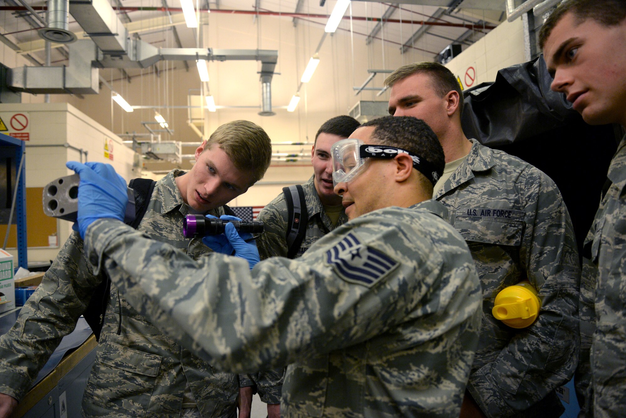U.S. Air Force Tech. Sgt. Alton Lee, center, 100th Maintenance Squadron NCO in charge of non-destructive inspections from Virginia Beach, Va., uses a black light to demonstrate the NDI process to U.S. Air Force Academy cadets during their tour of the section June 15, 2015, on RAF Mildenhall, England. Lee explained that imperfections would be practically invisible without the black light, giving the cadets a better understanding of how important the NDI section is to the maintenance of mission-essential aircraft. (U.S. Air Force photo by Senior Airman Kate Thornton/Released)