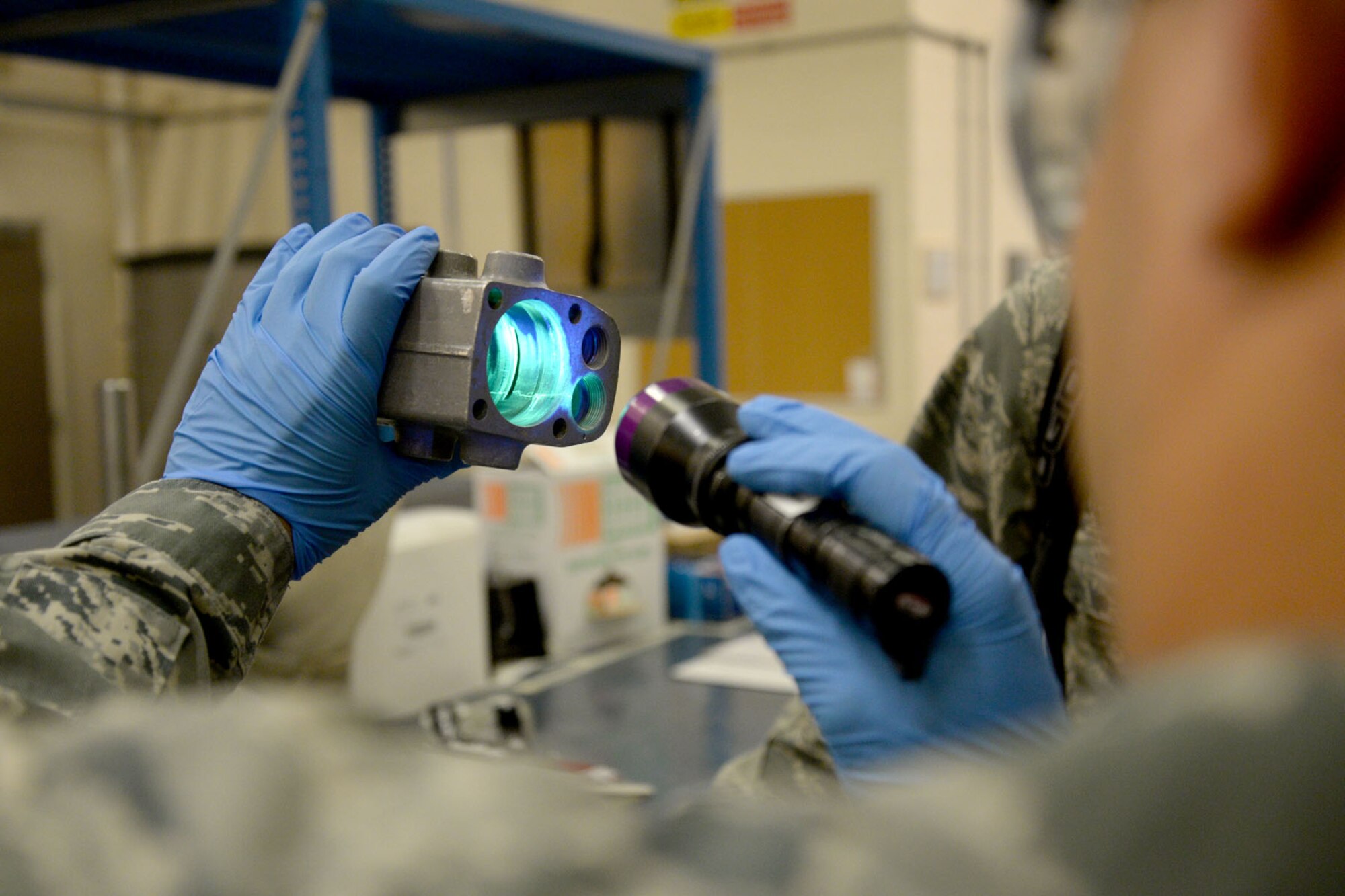 U.S. Air Force Tech. Sgt. Alton Lee, 100th Maintenance Squadron NCO in charge of non-destructive inspections from Virginia Beach, Va., uses a black light to show imperfections on an aircraft part to U.S. Air Force Academy cadets during their tour of the section June 15, 2015, on RAF Mildenhall, England. Lee explained that imperfections would be practically invisible without the black light, giving the cadets a better understanding of how important the NDI section is to the maintenance of mission-essential aircraft. (U.S. Air Force photo by Senior Airman Kate Thornton/Released)