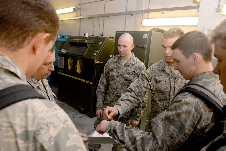 U.S. Air Force Academy cadets learn about plastic media, an abrasive blasting element used to strip paint from metal, as part of their tour around the 100th Maintenance Squadron fabrication section June 15, 2015, on RAF Mildenhall, England. The cadets spent two weeks on base learning about the operational Air Force before beginning their junior year of the Academy to broaden their knowledge of their future careers, and give them firsthand experience with officers and enlisted personnel. (U.S. Air Force photo by Senior Airman Kate Thornton/Released)