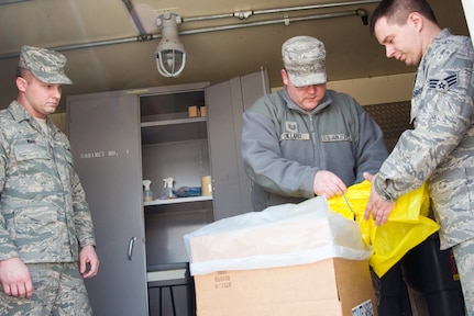 Air Force Staff Sgt. Patrick Ware, Air Force Tech Sgt. Ben Dillard, and Air Force Senior Airman Terry Whittington demonstrate procedures for handling regulated trash inside the designated regulated trash shed at the 167th Airlift Wing on April 1, 2011