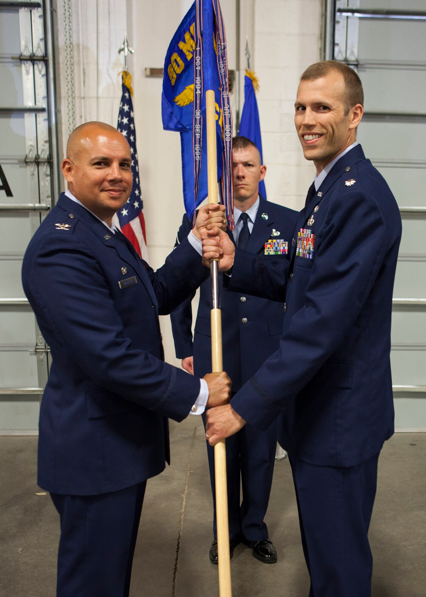 Col. Frank Verdugo, 90th Mission Support Group commander passes the guidon to Lt. Col. Robert C. Lance, 90th Civil Engineer Squadron commander, during the 90th CES change-of-command ceremony June 22, 2015, as Master Sgt. Christopher Gilmore, 90th CES first sergeant,    stands in the background in the Tech. Sgt. Matthew Schwartz Explosive Ordnance Disposal Facility on F.E. Warren Air Force Base, Wyo. The ceremony signified the transition of command from Lt. Col. James S. Duke to Vance. (U.S. Air Force Photo by Lan Kim)