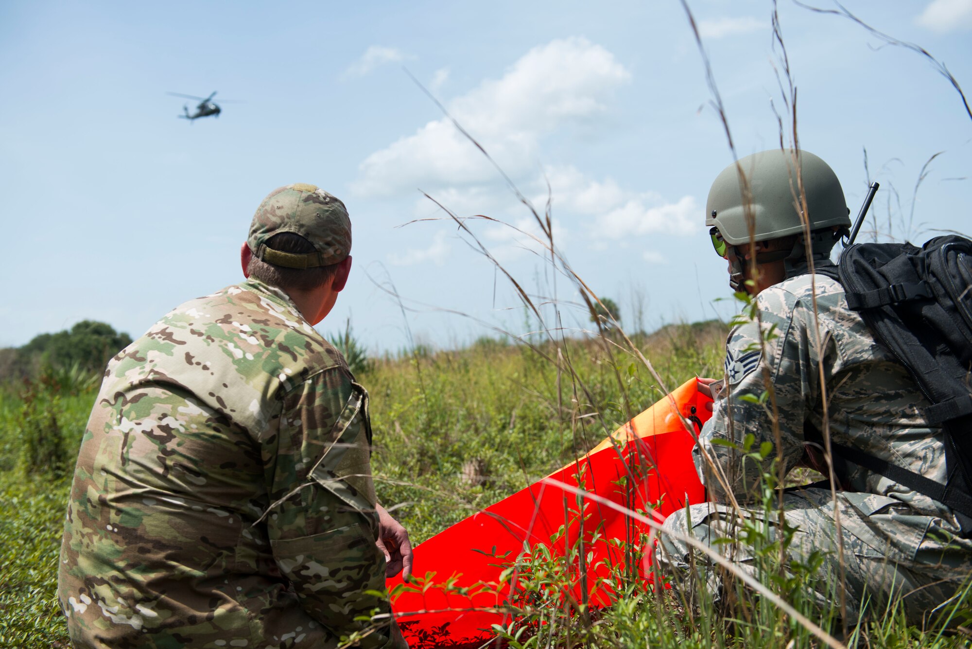U.S. Air Force Staff Sgt. Ryan Hall, left, 18th Air Support Operations Group Survival, Escape, Resistance and Evasion specialist, helps Senior Airman Michael Cruz, 23d Operations Support Squadron targets intelligence specialist, signal an HH-60G Pave Hawk during a personnel recovery scenario for Exercise DRAGON STRIKE June 11, 2015, near Avon Park Air Force Range, Fla. Hall and Cruz utilized a VS-17 panel, a specialized signaling device, to highlight their location. (U.S. Air Force photo by Airman 1st Class Dillian Bamman/Released)