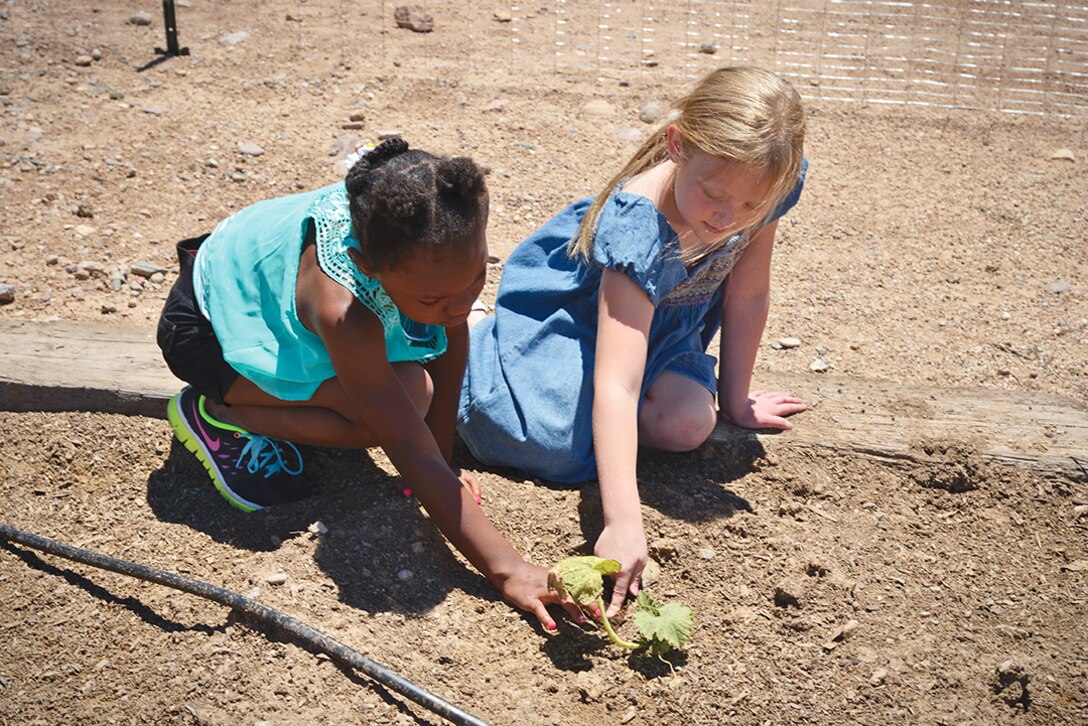 Zoe Mangrum and Hannah Graham check the soil moisture in the Youth Center garden.  The Youth Center is giving young folks at Kirtland a good foundation in gardening through the center’s Garden Club. (Photo by Jamie Burnett)