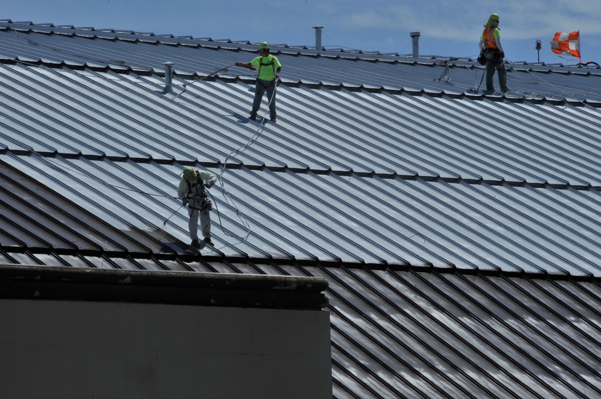 Contractors paint the maintenance hangar’s roof June 18, 2015, at Fairchild Air Force Base, Wash. In addition to painting the roof, the contractors also went over all the screws and panels, ensuring the roof is in the best condition. The new coating has a 15-year warranty and will save the Air Force $8 million. (U.S. Air Force photo/Airman 1st Class Taylor Bourgeous)