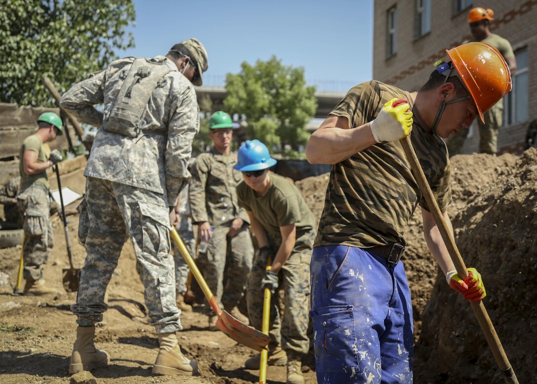 Mongolian Armed Forces Sgt. Erdenebayar Munkhchuluun, right, assists U.S. Marines and the U.S. Army with digging a hole to base a cement footer for a retention wall for the 55th Special Needs School during Khaan Quest 2015, in Ulaanbaatar, Mongolia, June 17, 2015. Khaan Quest is a regularly scheduled, multinational exercise hosted annually by Mogolian Armed Forces and co-sponsored by U.S. Army, Pacific, and U.S. Marine Corps Forces, Pacific. KQ15 is the latest in a continuing series of exercises designed to promote regional peace and security. This year marks the 13th iteration of this training event.