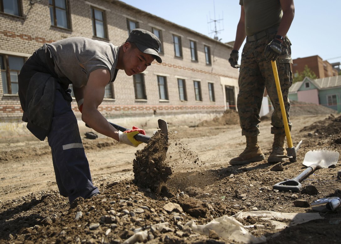 Mongolian Armed Forces Junior Sgt. Sube Batsumberel, left, assists U.S. Marine Corps Lance Cpl. Cole Street, right, with 9th Engineer Support Battalion, 3rd Marine Logistics Group Alpha Company, in digging holes for the base of fence posts surrounding the basketball court for the 55th Special Needs School during Khaan Quest 2015, in Ulaanbaatar, Mongolia, June 17, 2015. Khaan Quest is a regularly scheduled, multinational exercise hosted annually by Mongolian Armed Forces and co-sponsored by U.S. Army, Pacific, and U.S. Marine Corps Forces, Pacific. KQ15 is the latest in a continuing series of exercises designed to promote regional peace and security. This year marks the 13th iteration of this training event.