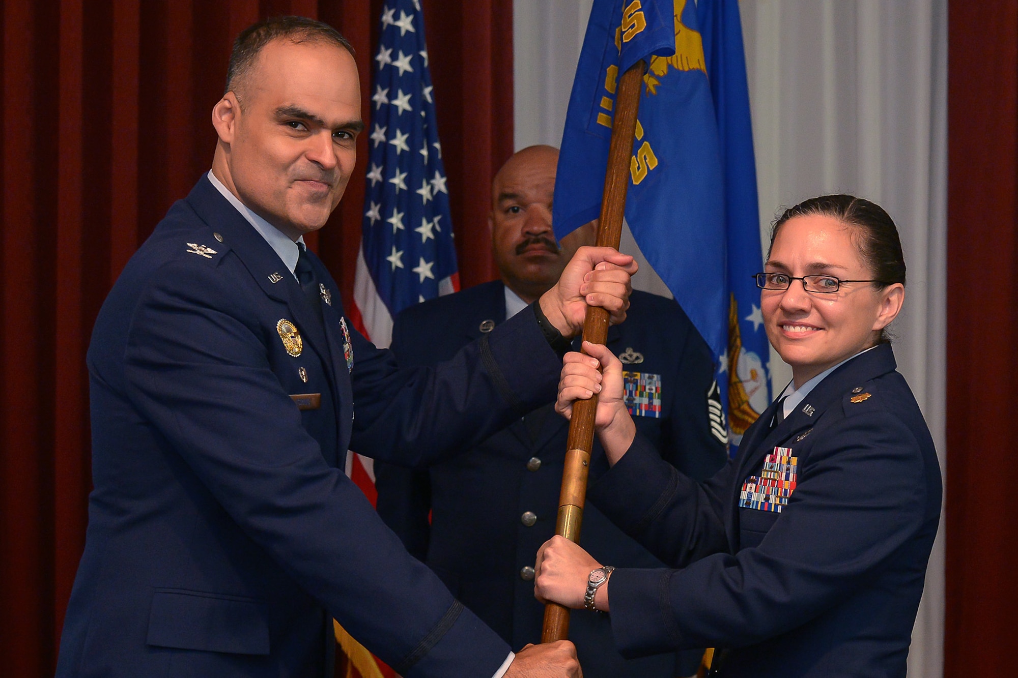 Col. Eric Espino (left), 360th Recruiting Group commander, passes the flag to Maj. Amy Goff, 319th Recruiting Squadron commander, during the squadron's change of command ceremony June 23 at the Minuteman Commons as Master Sgt. Kevin Walker looks on. The squadron directs and operates the recruiting activities of eight enlisted accession flights and one line officer accession flight for Connecticut, Maine, Massachusetts, New Hampshire, Rhode Island, Vermont and Europe. (U.S. Air Force photo by Walter Santos) 