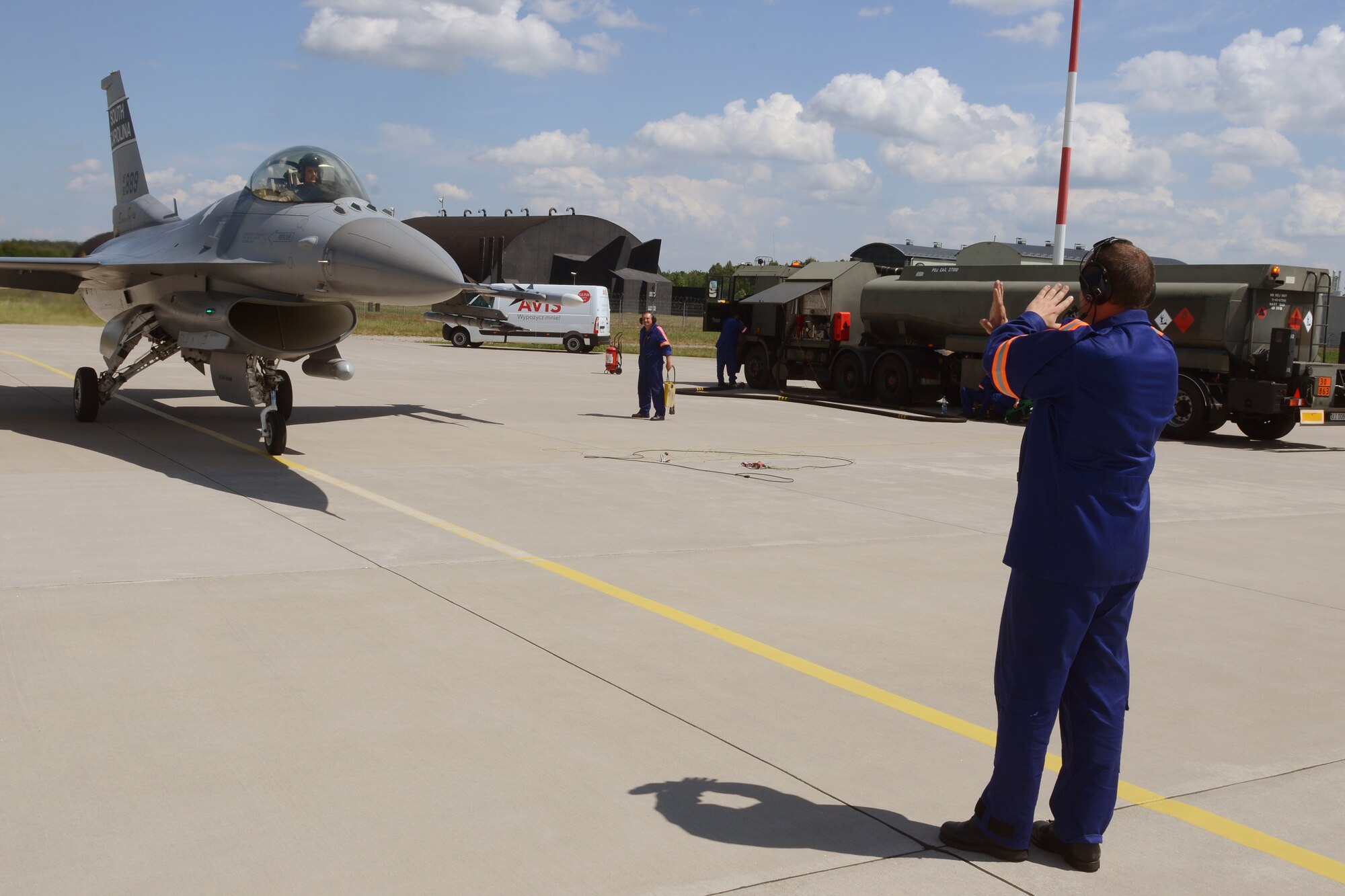 Polish air force Warrant Officer Witold Bukowiec, from the 32nd Tactical Air Base at Łask Air Base, Poland, marshals a South Carolina Air National Guard F-16 fighter jet, piloted by Capt. Mark "Dirty" Fattman, to be "hot-pit" refueled, June 1, 2015. F-16 aircraft maintenance crews from the Polish 32nd Tactical Air Base and the South Carolina Air National Guard's 169th Fighter Wing teamed-up to conduct "hot-pit" refueling at Łask Air Base, Poland, June 1, 2015. The 32nd Tactical Air Base was recently certified to perform "hot-pit" refueling, which involves refueling a recently landed F-16 so that it can take off for another mission without stopping its engine. Three units worked together to learn "hot-pitting" techniques from each other as well as offering opportunities for Polish Airmen to learn from the more seasoned 169th Fighter Wing and 52d Fighter Wing maintainers. U.S. Air Force Airmen from Spangdahlem Air Base, Germany and the South Carolina Air National Guard’s 169th Fighter Wing from McEntire Joint National Guard Base, are deployed to Łask Air Base in support of Operation Atlantic Resolve, during the month of June. These training missions, called Aviation Detachment Rotations, pair U.S. fighter pilots and maintenance crews with their Polish Air Force counterparts at Łask Air Base, during Operation Atlantic Resolve. This bilateral training, hosted by permanently assigned USAF service members assigned to Poland, has taken place since 2012. Through strengthened relationships and engagements with our allies, the U.S. and NATO demonstrate their shared commitment to a peaceful, stable and secure Europe. (South Carolina Air National Guard photo by Senior Master Sgt. Edward Snyder / RELEASED)