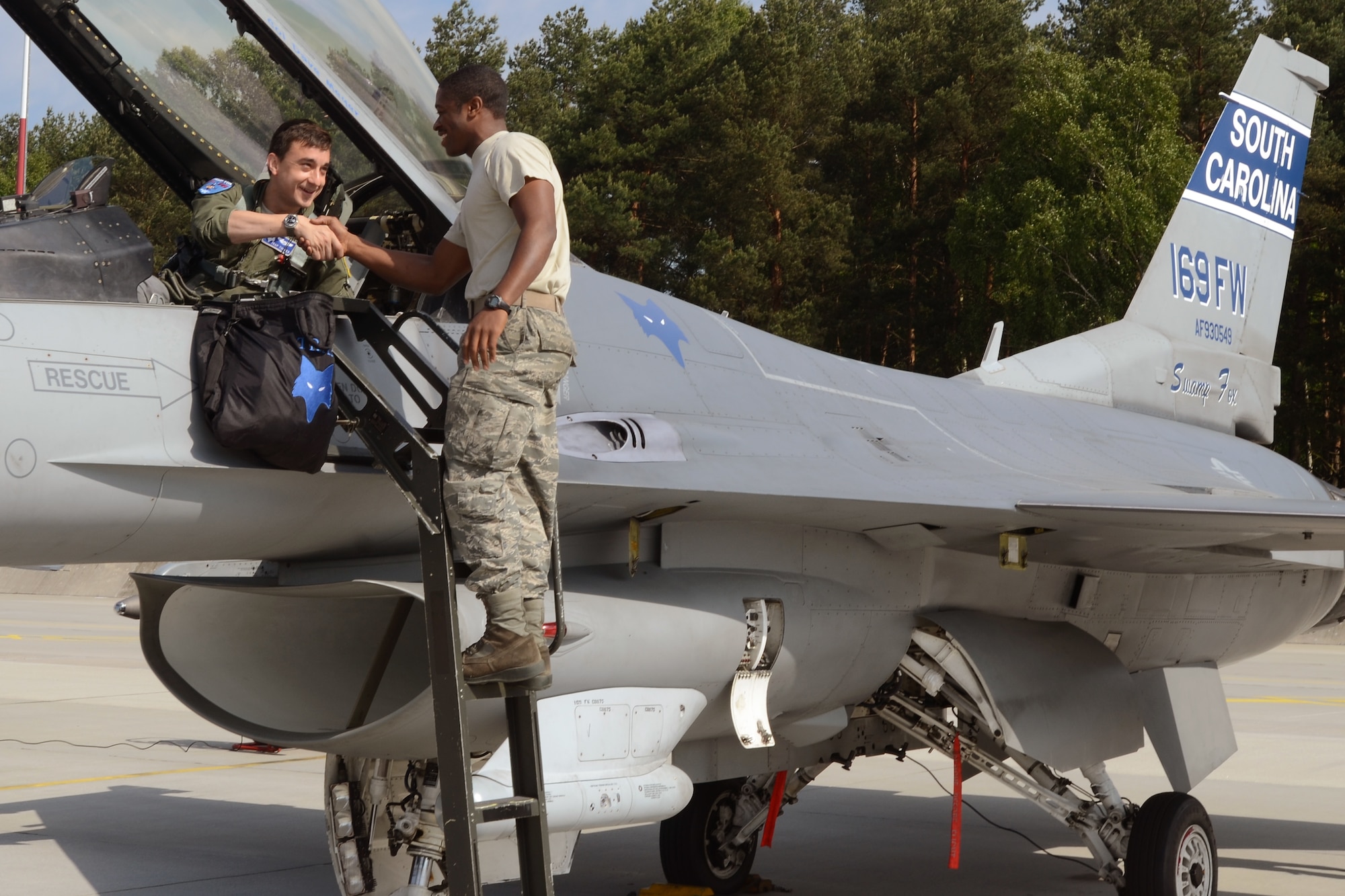 U.S. Air Force Capt. Lance "Trap" Tucker (center), a pilot assigned to the 157th Fighter Squadron, thanks Airman 1st Class Warren Gallman, a crew chief assigned to the 169th Aircraft Maintenance Squadron, for a clean, "CODE 1" F-16 as he prepares for his first mission in support of Operation Atlantic Resolve at Łask Air Base, Poland, June 1, 2015. U.S. Air Force Airmen from the South Carolina Air National Guard’s 169th Fighter Wing from McEntire Joint National Guard Base, are deployed to Łask Air Base in support of Operation Atlantic Resolve, during the month of June. The training mission, called an Aviation Detachment Rotation, will pair Swamp Fox F-16 pilots and maintenance crews with their Polish Air Force counterparts at Łask Air Base, during Operation Atlantic Resolve. This bilateral training, held by U.S. Air Forces Europe and Air Forces Africa, has taken place since 2012. Through strengthened relationships and engagements with our allies, the U.S. and NATO demonstrate their shared commitment to a peaceful, stable and secure Europe. (South Carolina Air National Guard photo by Senior Master Sgt. Edward Snyder / RELEASED)