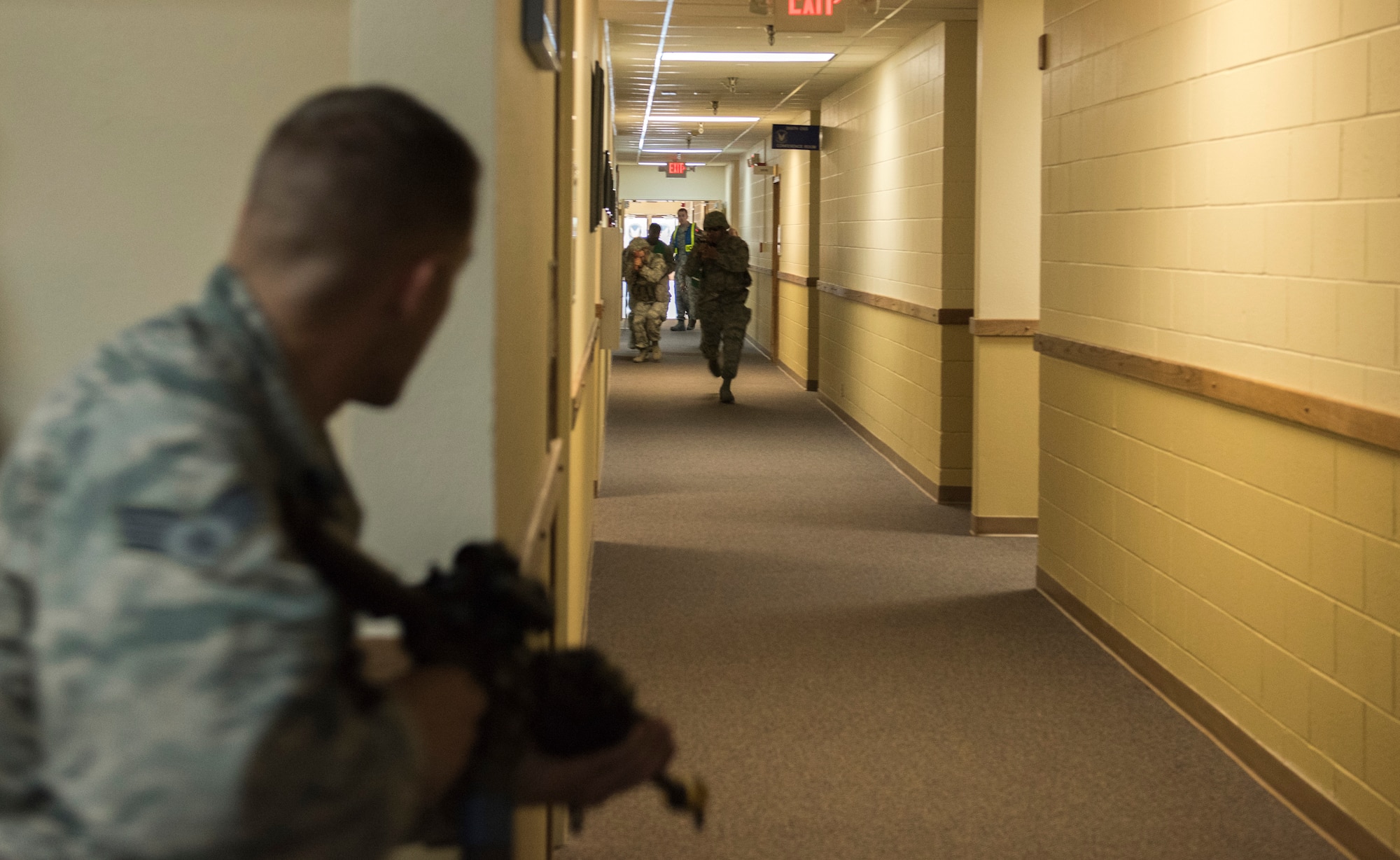 Senior Airman Kyle Honeycutt, role-playing an active shooter, stares down the hall as Security Forces members race towards him during the exercise June 18, 2015, at Mountain Home Air Force Base, Idaho. A call was made to Security Forces moments after the first "shots" were fired. (U.S. Air Force photo by Airman 1st Class Jeremy L. Mosier/RELEASED)