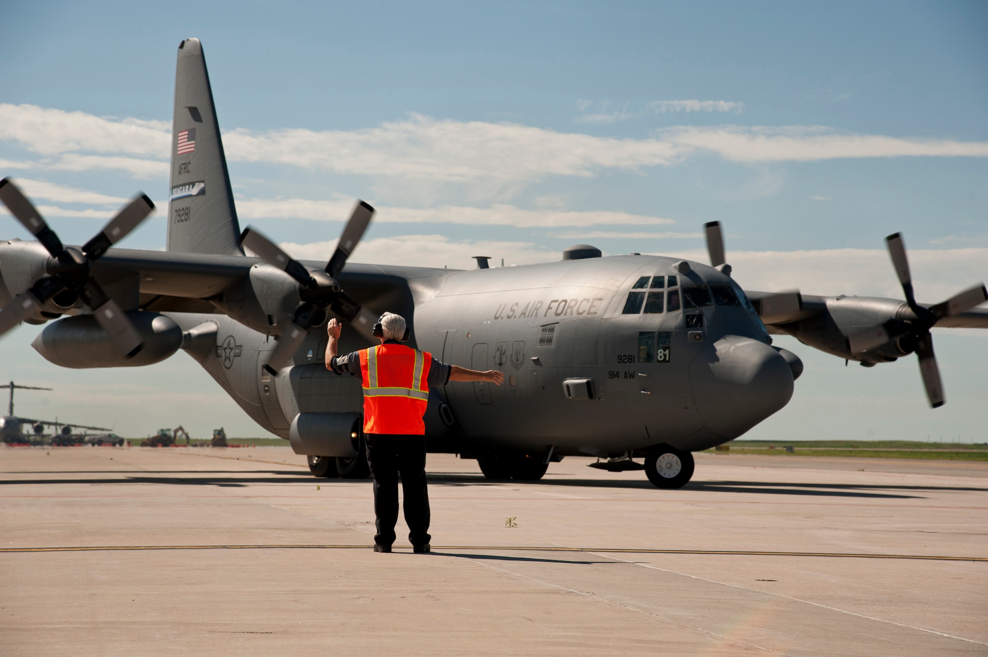PETERSON AIR FORCE BASE, Colo. – Chuck Fettes, 21st Operations Support Squadron transient alert servicer, waves off an outgoing C-130H on June 17, 2015. Fettes is part of a nine member servicing crew who escorts, coordinates services, fuels, and supports all aircraft to and from Peterson. (U.S. Air Force photo by Senior Airman Tiffany DeNault)