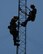 Airman 1st Class Mark Dunton (left) and Senior Airman Samantha Maquillan are silhouetted against the late morning sun as they work on upgrading lightning protection and grounding on a communications tower at Pease Air National Guard Base, N.H., on June 22, 2015. The installation of the lightning protection gear helps protect resources such as radios that 157th Air Refueling Wing Airmen use to support the mission. The Airmen are assigned to the 243rd Engineering Installation Squadron, Maine Air National Guard in South Portland, Maine.  (U.S. Air National Guard photo by Staff Sgt. Curtis J. Lenz)