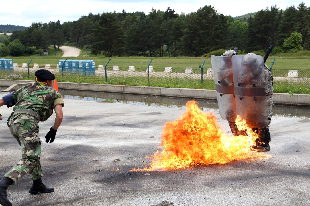 U.S. soldiers move through fire as a Portuguese soldier, left, throws a Molotov cocktail during a fire phobia exercise at the Joint Multinational Readiness Center in Hohenfels, Germany, June 16, 2015.