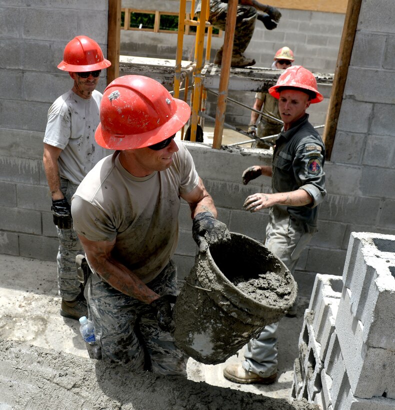U.S. Air Force Master Sgt. Isaiah Maki hands a bucket of cement to U.S. Air Force Staff Sgt. Dustin Haycox as they help build a two-room classroom in Ocotes Alto, Honduras, June 22, 2015. 