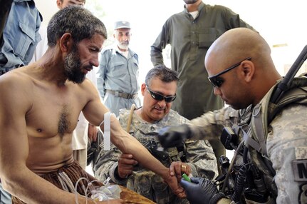 Spc. Daniel Kersbergen, security forces team member with the Iowa National Guard's 734th Agribusiness Development Team, administers an intravenous fluids bag to Roz Amin, an injured Afghan road worker, as Army Staff Sgt. Michael Martinez, the ADT's senior combat medic, supervises at the Sarkani District Center April 25, 2011.