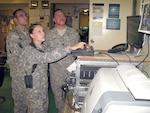 Spc. Joseph Deramo, left, and Spc. Xavier Flores, right, look on as Army Pfc. Audrey Triplett monitors input from one of three 107-foot Rapid Aerostat Initial Deployment towers and eight other sites the 164th Air Defense Artillery operates to provide force protection at Bagram Airfield, Afghanistan, and for troops operating outside the wire.