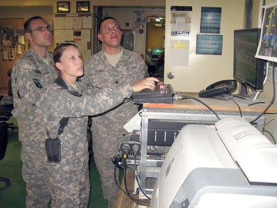 Spc. Joseph Deramo, left, and Spc. Xavier Flores, right, look on as Army Pfc. Audrey Triplett monitors input from one of three 107-foot Rapid Aerostat Initial Deployment towers and eight other sites the 164th Air Defense Artillery operates to provide force protection at Bagram Airfield, Afghanistan, and for troops operating outside the wire.