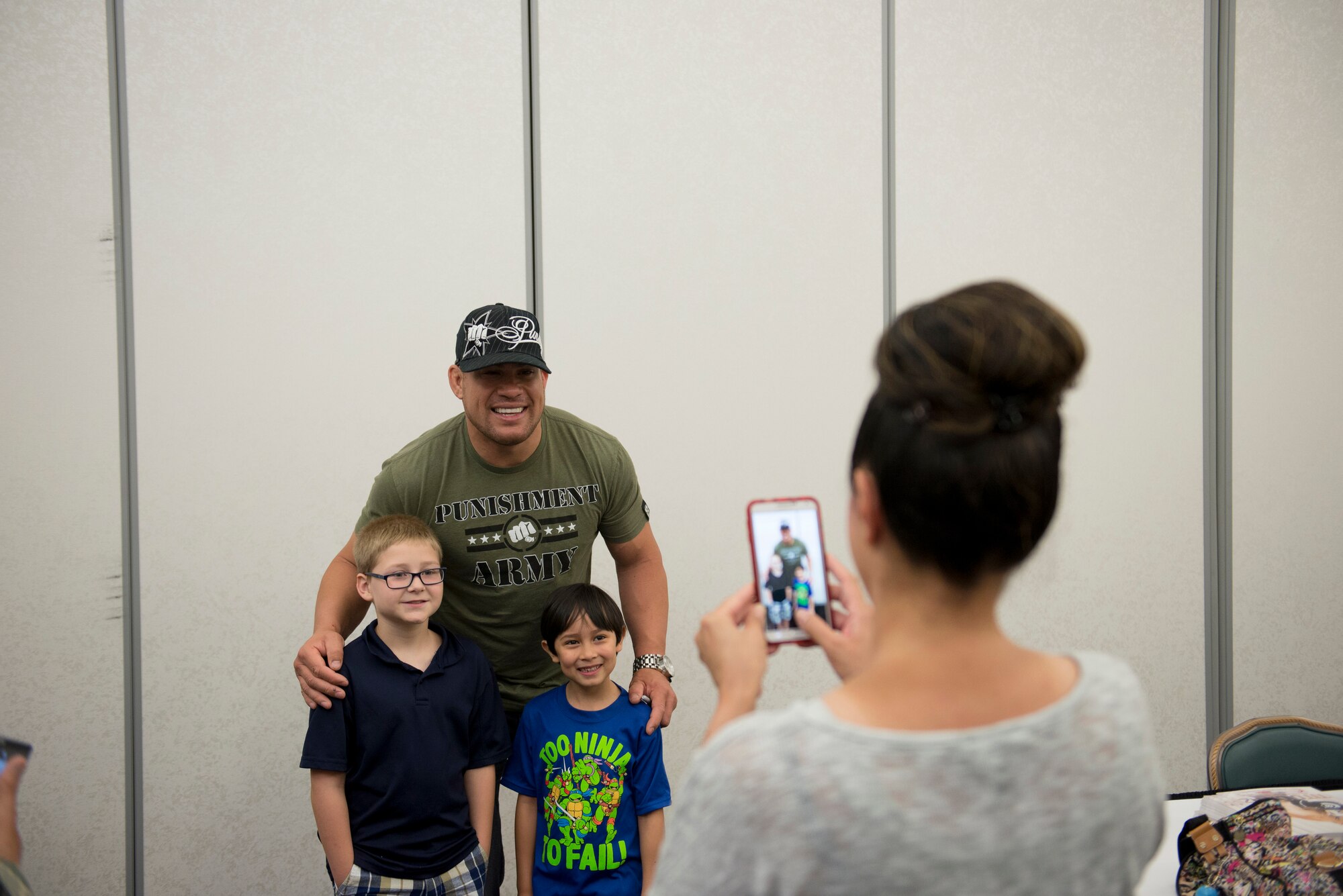 Tito Ortiz and two fans pose for a photo during a meet and great with fans at the Scott Club, Scott Air Force Base, Illinois, June 17, 2015. Ortiz and three other Mixed Martial Arts Bellator fighters visited Scott to meet and sign autographs, take a tour of a C-21 and work out with Airmen. (U.S. Air Force Photo by Airman 1st Class Megan Friedl)