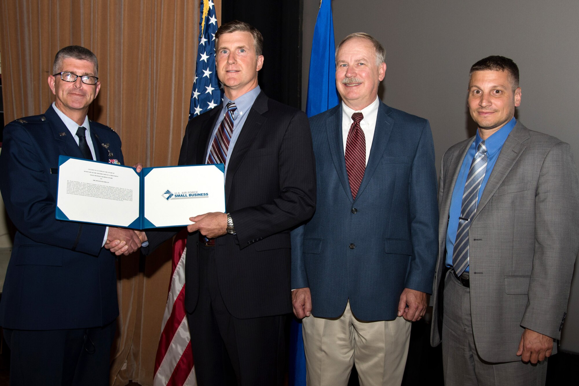 U.S. Air Force Col. Scott Owens, Theater Battle Control Division senior materiel leader, presents Don MacMillan, PEITSS program manager, with an Air Force-level Small Business Programs award during a division meeting at Hanscom Air Force Base, Mass., June 24, 2015. MacMillan's unique approach and extensive market research resulted in good news for small business contractors vying for the PEITSS contract -- a contract previously deemed large business worthy. Also on stage is Bill Donaldson, Hanscom Small Business director, and Rob Bubello (far right), MacMillan's supervisor. (U.S. Air Force photo by Mark Herlihy)  