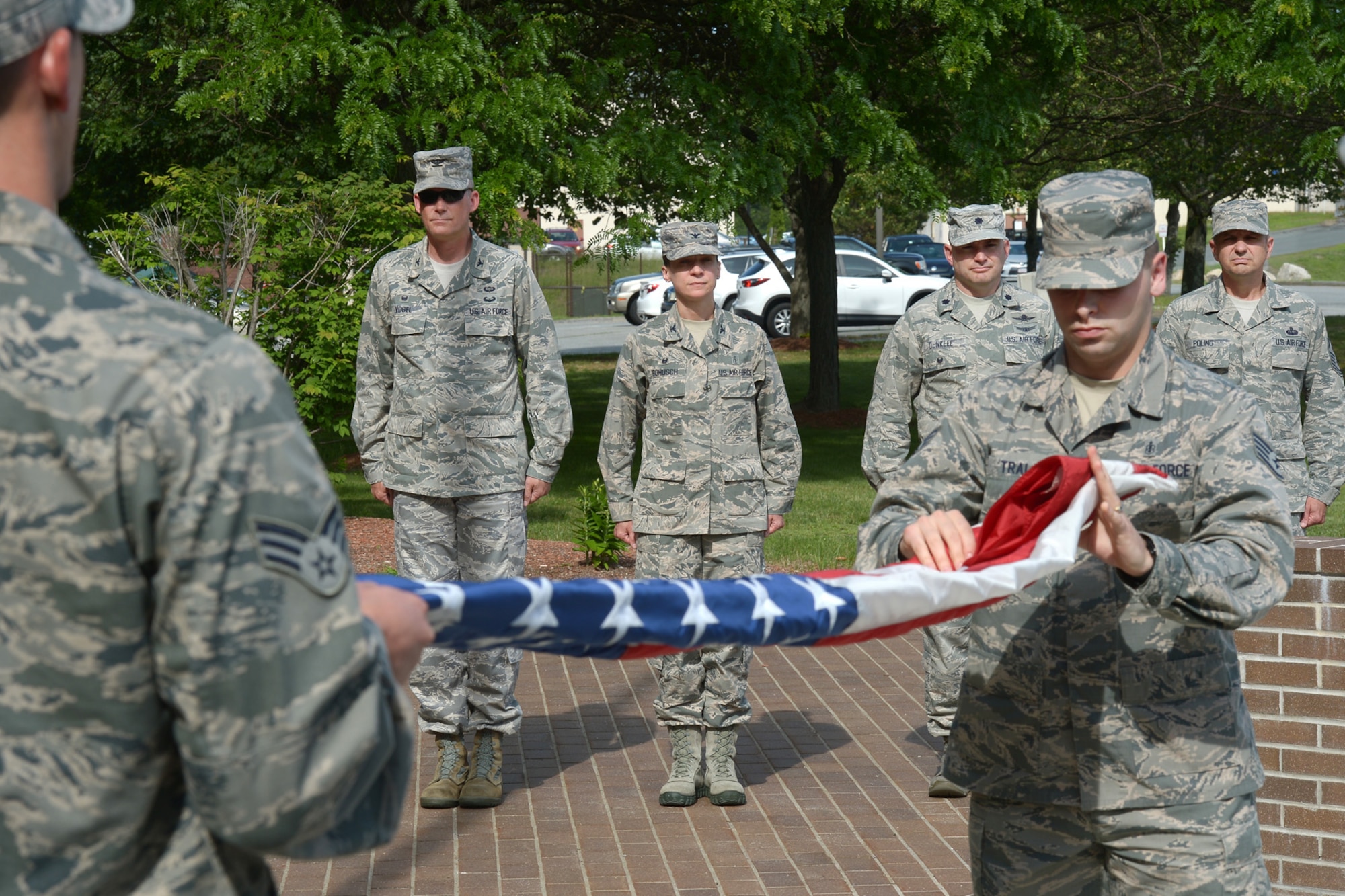 Senior Airman Gary Dennis (left) and Staff Sgt. Michael Trala, both assigned to the 66th Medical Squadron, fold the flag under the watchful eye of (left to right) Col. Michael A. Vogel, 66th Air Base group commander; Col. Therese A. Bohusch, 66 MDS commander; Lt. Col. David R. Dunklee, 66 ABG deputy commander; and Hanscom Command Chief Master Sgt. Craig A. Poling during a formal retreat ceremony outside Building 1305, June 18. Members of 66 MDS participated in the retreat ceremony by retrieving the flag and providing a flight of clinic personnel. (U.S. Air Force photo by Jerry Saslav) 