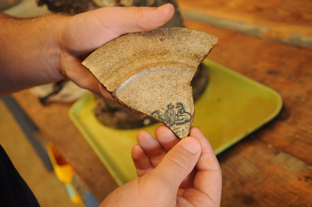 Parker Brooks, a conservator and graduate student from Texas A&M University’s Conservation Research Laboratory, holds a piece of pottery recovered from the CSS Georgia. Archaeologists are using the portions of the writing from pieces like this to determine its origin and age. Some pottery recovered from the site was created before Europeans arrived in North America.