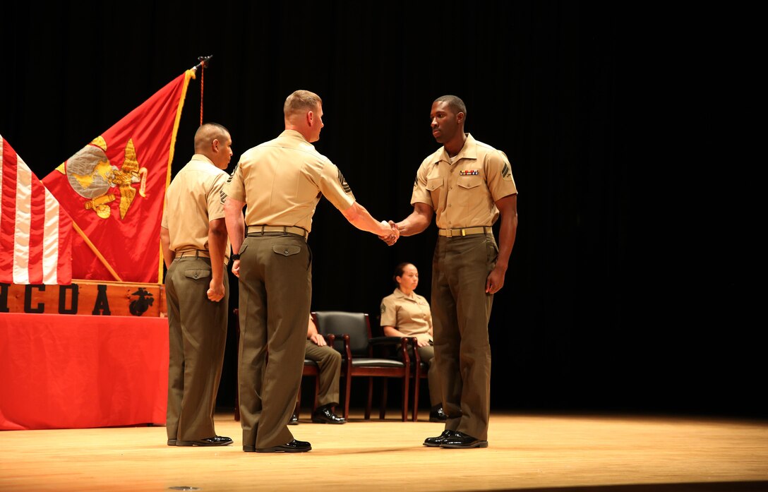 Cpl. Giovanni D. Destin, right, rifleman, Company A, Ground Combat Element Integrated Task Force, is congratulated by 1st Sgt. John D. Dober, center, first sergeant, Co. A, GCEITF, and guest speaker, during the Corporal’s Course graduation at the Marine Corps Base Camp Lejeune Theater, June 24, 2015. From October 2014 to July 2015, the GCEITF conducted individual and collective level skills training in designated ground combat arms occupational specialties in order to facilitate the standards-based assessment of the physical performance of Marines in a simulated operating environment performing specific ground combat arms tasks. (U.S. Marine Corps photo by Cpl. Paul S. Martinez/Released) 