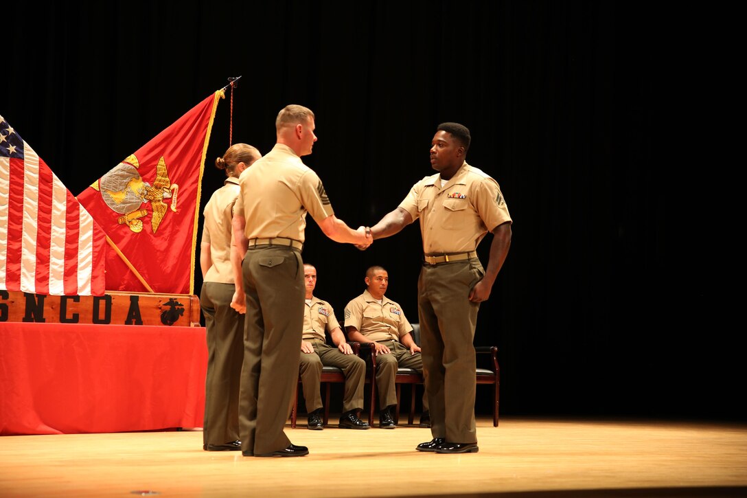 Cpl. Matiyes Kinker, right, assaultman, Weapons Company, Ground Combat Element Integrated Task Force, is congratulated by 1st Sgt. John D. Dober, center, first sergeant, Company A, GCEITF, and guest speaker, during the Corporal’s Course graduation at the Marine Corps Base Camp Lejeune Theater, June 24, 2015. From October 2014 to July 2015, the GCEITF conducted individual and collective level skills training in designated ground combat arms occupational specialties in order to facilitate the standards-based assessment of the physical performance of Marines in a simulated operating environment performing specific ground combat arms tasks. (U.S. Marine Corps photo by Cpl. Paul S. Martinez/Released) 