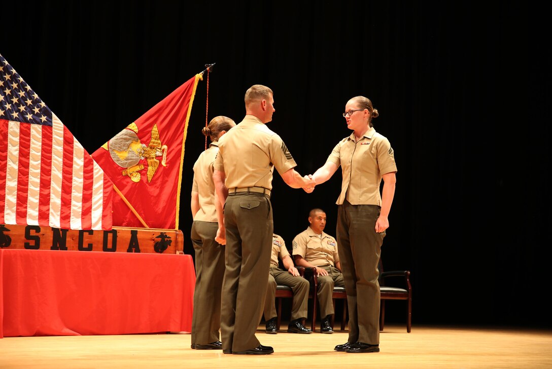 Cpl. Katie M. Gorz, right, rifleman, Company A, Ground Combat Element Integrated Task Force, is congratulated by 1st Sgt. John D. Dober, center, first sergeant, Co. A, GCEITF, and guest speaker, during the Corporal’s Course graduation at the Marine Corps Base Camp Lejeune Theater, June 24, 2015. From October 2014 to July 2015, the GCEITF conducted individual and collective level skills training in designated ground combat arms occupational specialties in order to facilitate the standards-based assessment of the physical performance of Marines in a simulated operating environment performing specific ground combat arms tasks. (U.S. Marine Corps photo by Cpl. Paul S. Martinez/Released) 