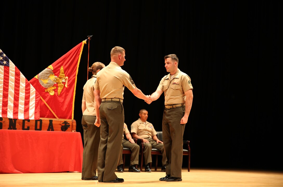 Cpl. Thomas P. Gray, right, anti-tank missileman, Weapons Company, Ground Combat Element Integrated Task Force, is congratulated by 1st Sgt. John D. Dober, center, first sergeant, Company A, GCEITF, and guest speaker, during the Corporal’s Course graduation at the Marine Corps Base Camp Lejeune Theater, June 24, 2015. From October 2014 to July 2015, the GCEITF conducted individual and collective level skills training in designated ground combat arms occupational specialties in order to facilitate the standards-based assessment of the physical performance of Marines in a simulated operating environment performing specific ground combat arms tasks. (U.S. Marine Corps photo by Cpl. Paul S. Martinez/Released)