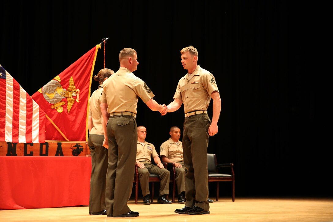 Cpl. Mark E. Miller, right, rifleman, Company A, Ground Combat Element Integrated Task Force, is congratulated by 1st Sgt. John D. Dober, center, first sergeant, Company A, GCEITF, and guest speaker, during the Corporal’s Course graduation at the Marine Corps Base Camp Lejeune Theater, June 24, 2015. From October 2014 to July 2015, the GCEITF conducted individual and collective level skills training in designated ground combat arms occupational specialties in order to facilitate the standards-based assessment of the physical performance of Marines in a simulated operating environment performing specific ground combat arms tasks. (U.S. Marine Corps photo by Cpl. Paul S. Martinez/Released) 