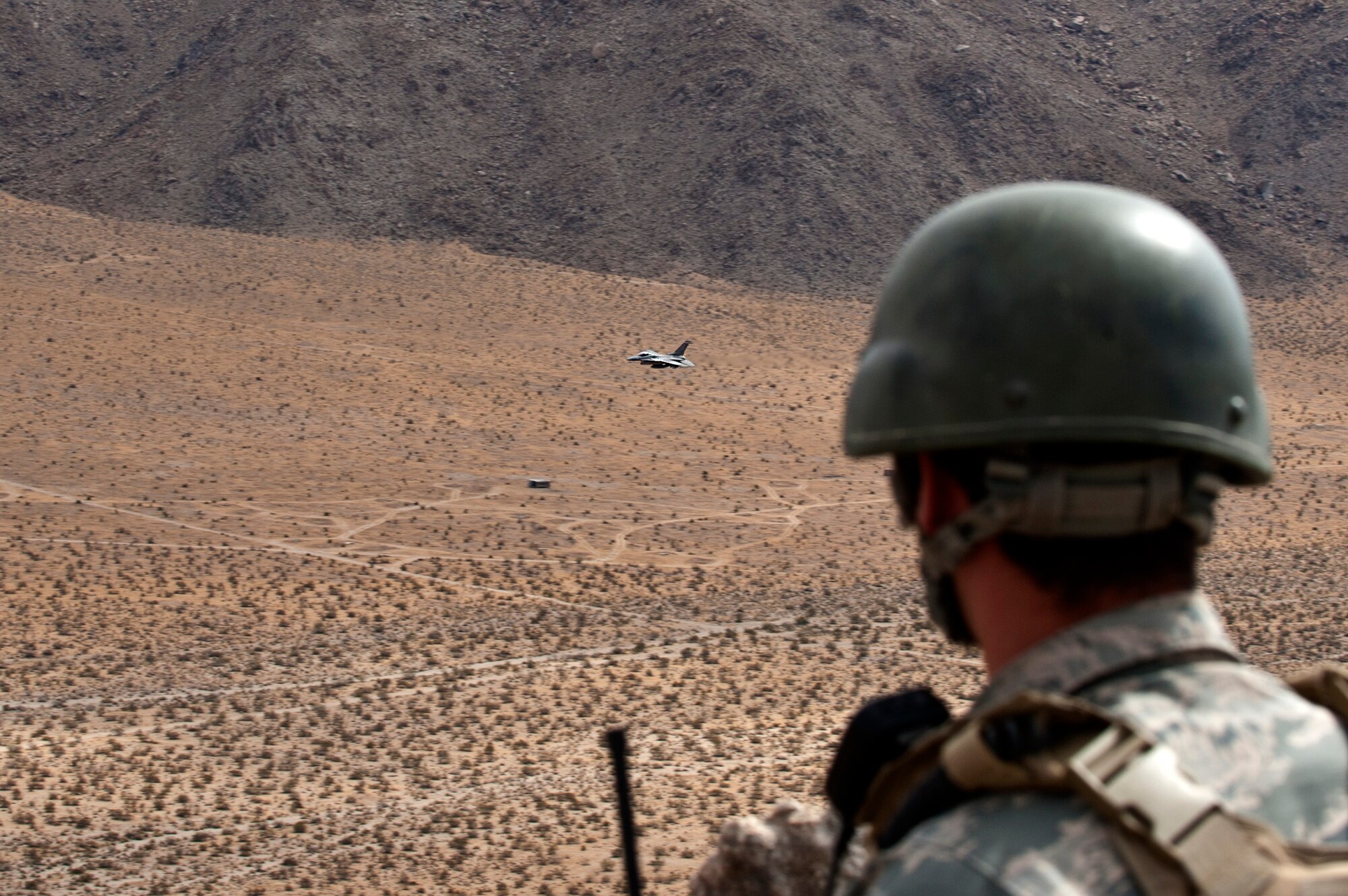 A tactical air control party Airman from the 7th Air Support Operations Squadron, Fort Bliss, Texas, looks on as an F-16 Fighting Falcon executes a “show of force” in the skies over the National Traning Center Range, Fort Irwin, Calif., during a Green Flag 15-08 training scenario June 12, 2015.  After an integrated attack maneuver combining fire from armored vehicles, artillery and aircraft alike, this display of air dominance can act as a deterrent for any remaining enemy combatants in the area. (U.S. Air Force photo by Senior Airman Joshua Kleinholz)