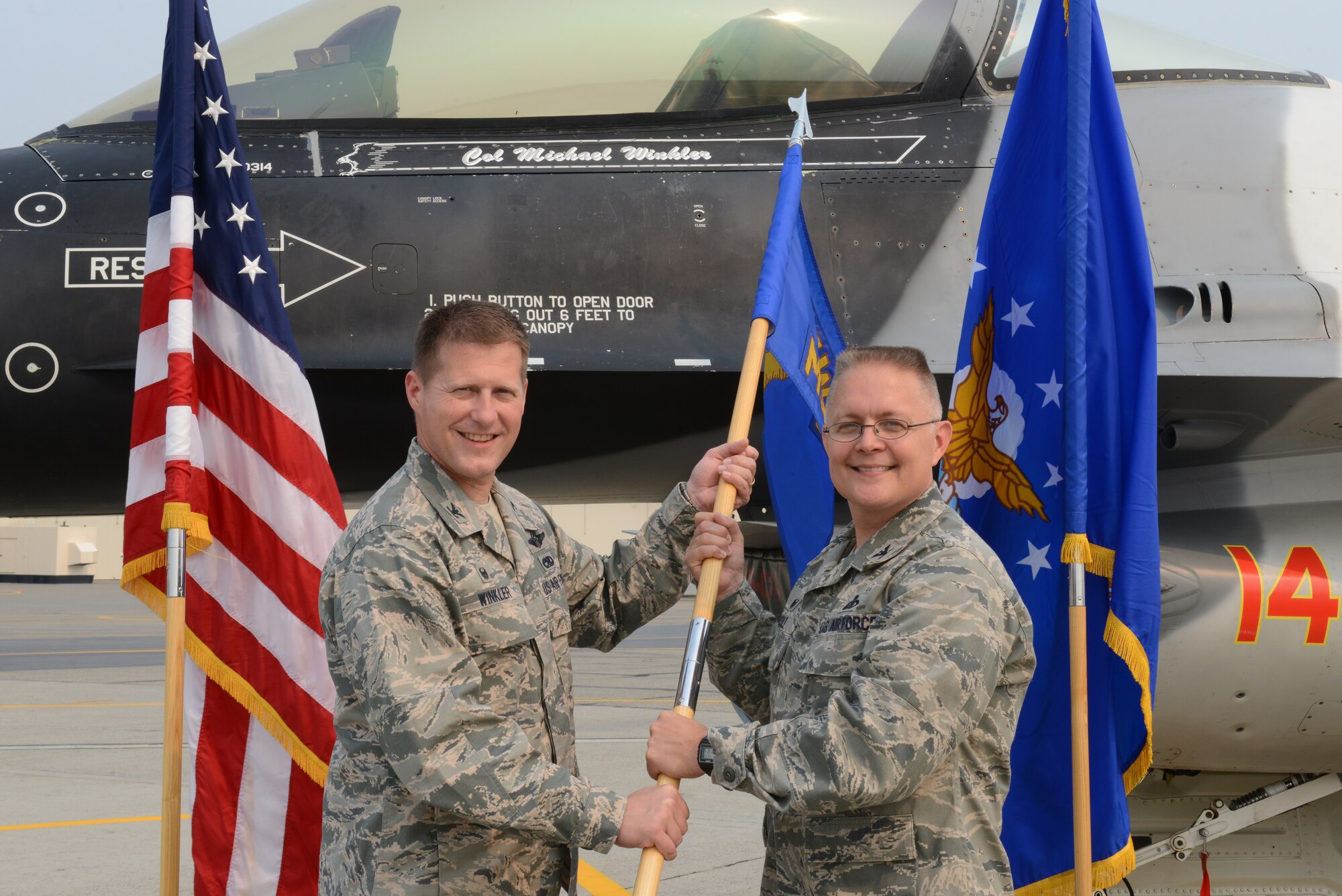 U.S. Air Force Col. Michael Winkler, the 354th Fighter Wing commander, passes the 354th Mission Support Group guidon to Col. Richard Cole, the new 354th MSG commander, in front of the command jet, an F-16 Fighting Falcon assigned to the 18th Aggressor Squadron, June 23, 2015, at Eielson Air Force Base, Alaska. Col. Larry Rice, the outgoing group commander, will move on to Randolph Air Force Base. (U.S. Air Force photo by Senior Airman Ashley Nicole Taylor/Released)
