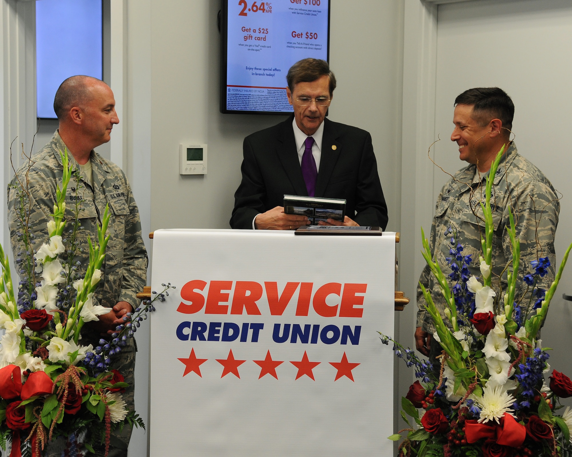 Gordon Simmons, President of Service Credit Union, presents Maj. Frank Burks, 319th Wing Staff Agencies commander and Col. Anthony Hernandez, 319th Mission Support Group commander with a New Hampshire photographic journey book during the grand opening of the permanent SCU branch on Grand Forks Air Force Base, N.D. on June 24, 2015. SCU first arrived at Grand Forks AFB in March, where its temporary office serviced base personnel before the grand opening of its main facility. (U.S. Air Force Photo by Senior Airman Zachiah Roberson/released)